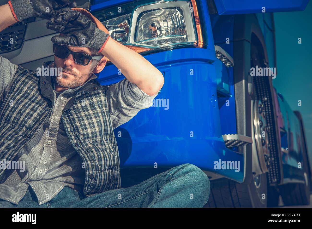 Stanco Caucasian Camionista nella sua 30s appoggiata nella parte anteriore della sua Semi trattore. Industria dei Trasporti concetto. Foto Stock