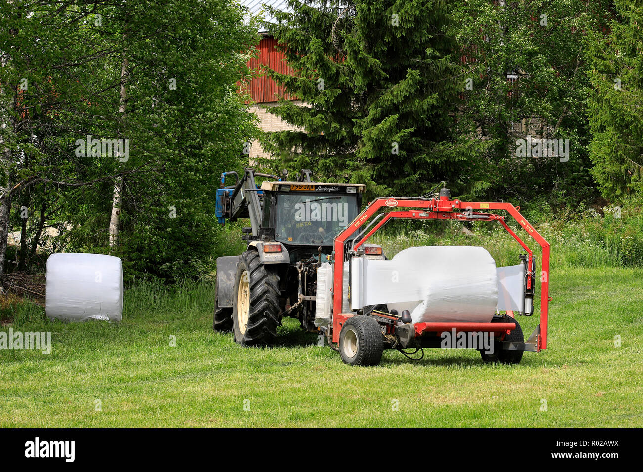 Uurainen, Finlandia - 15 Giugno 2018: confezionamento balle di fieno in pellicola plastica con Lamborghini trattore e Vicon BV 1700 wrapper satellitare del giorno d'estate. Foto Stock