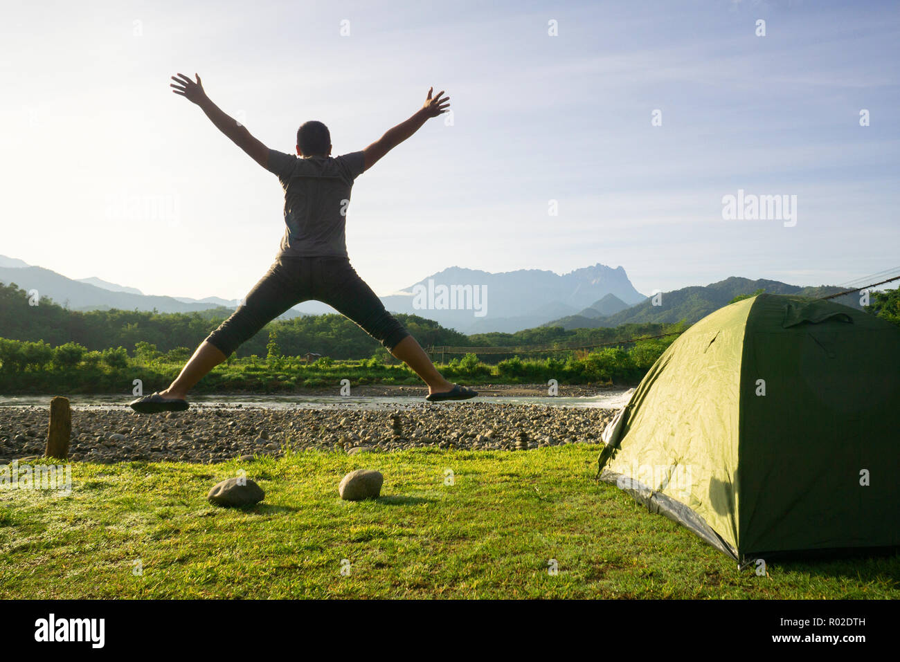 L'uomo saltando al campeggio con splendide montagne sullo sfondo. Foto Stock