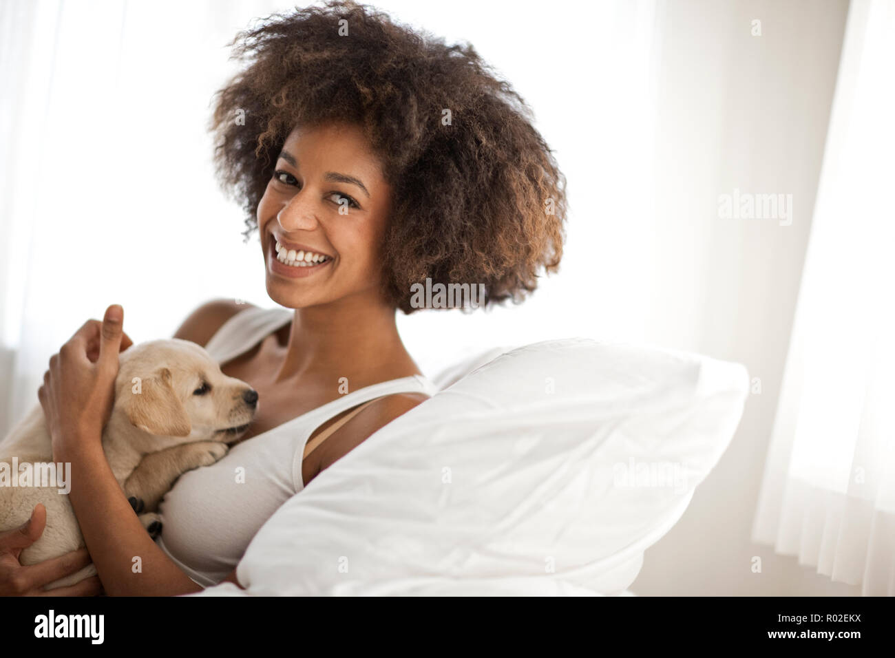 Donna pacche un cucciolo da seduto sul letto. Foto Stock