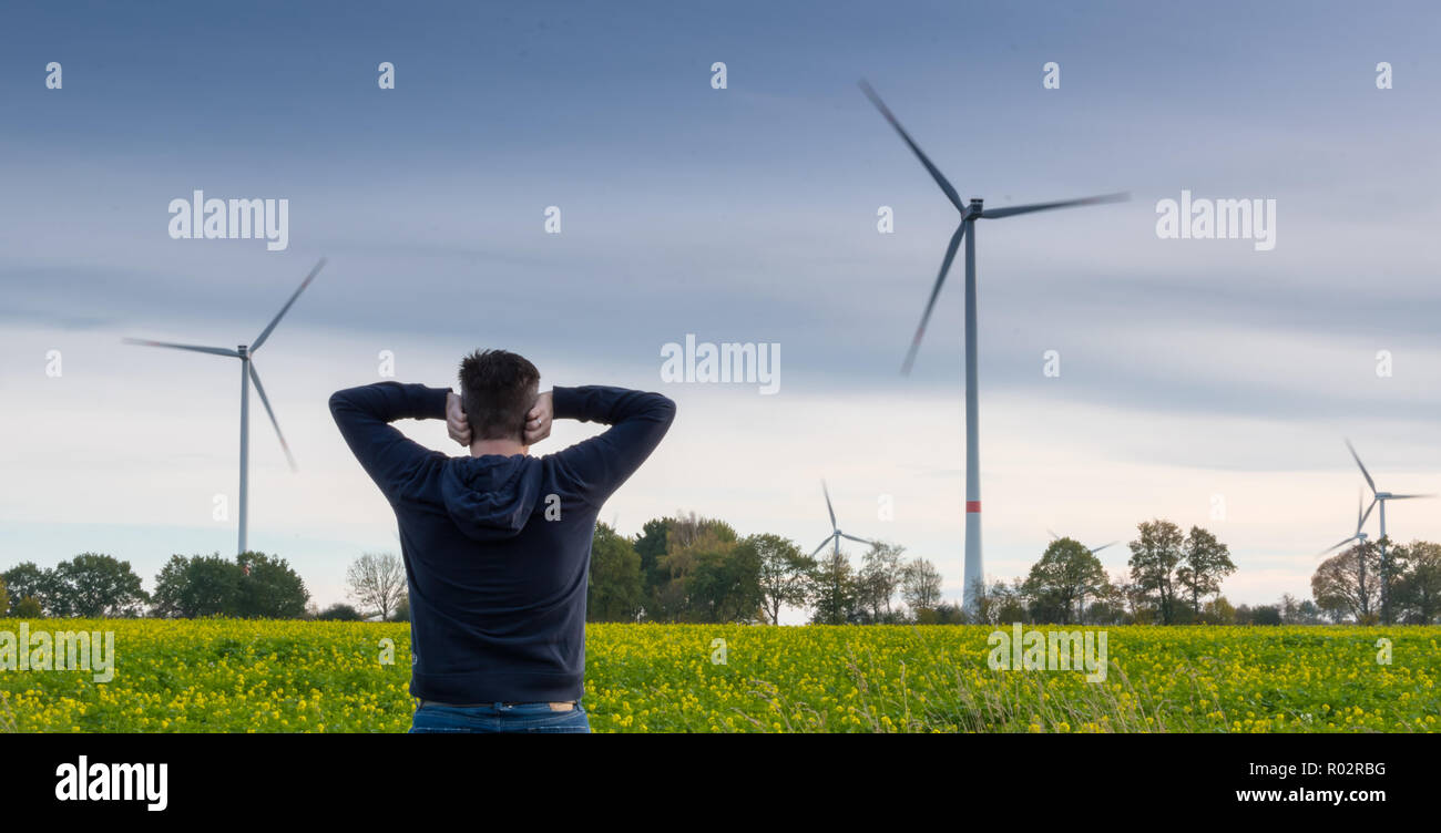 Uomo di fronte una fattoria eolica blocca i suoi orecchi per ridurre il rumore Foto Stock