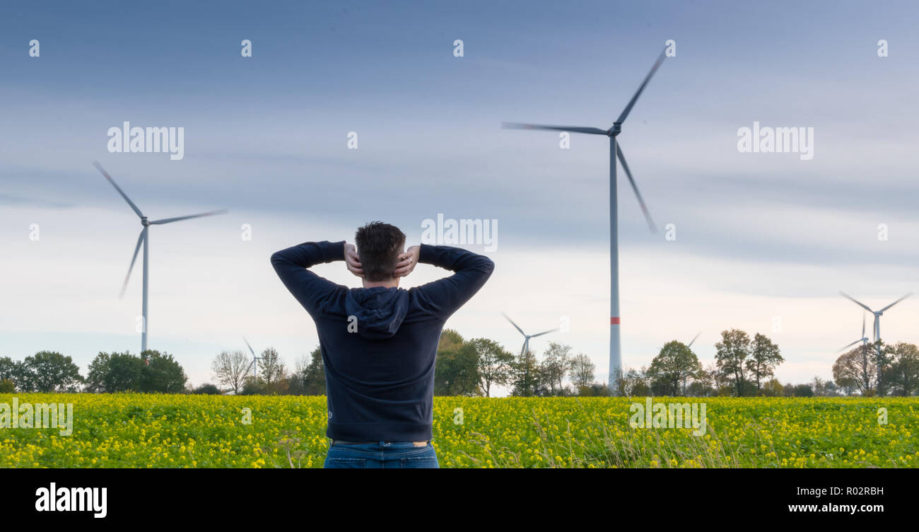 Uomo di fronte una fattoria eolica blocca i suoi orecchi per ridurre il rumore Foto Stock