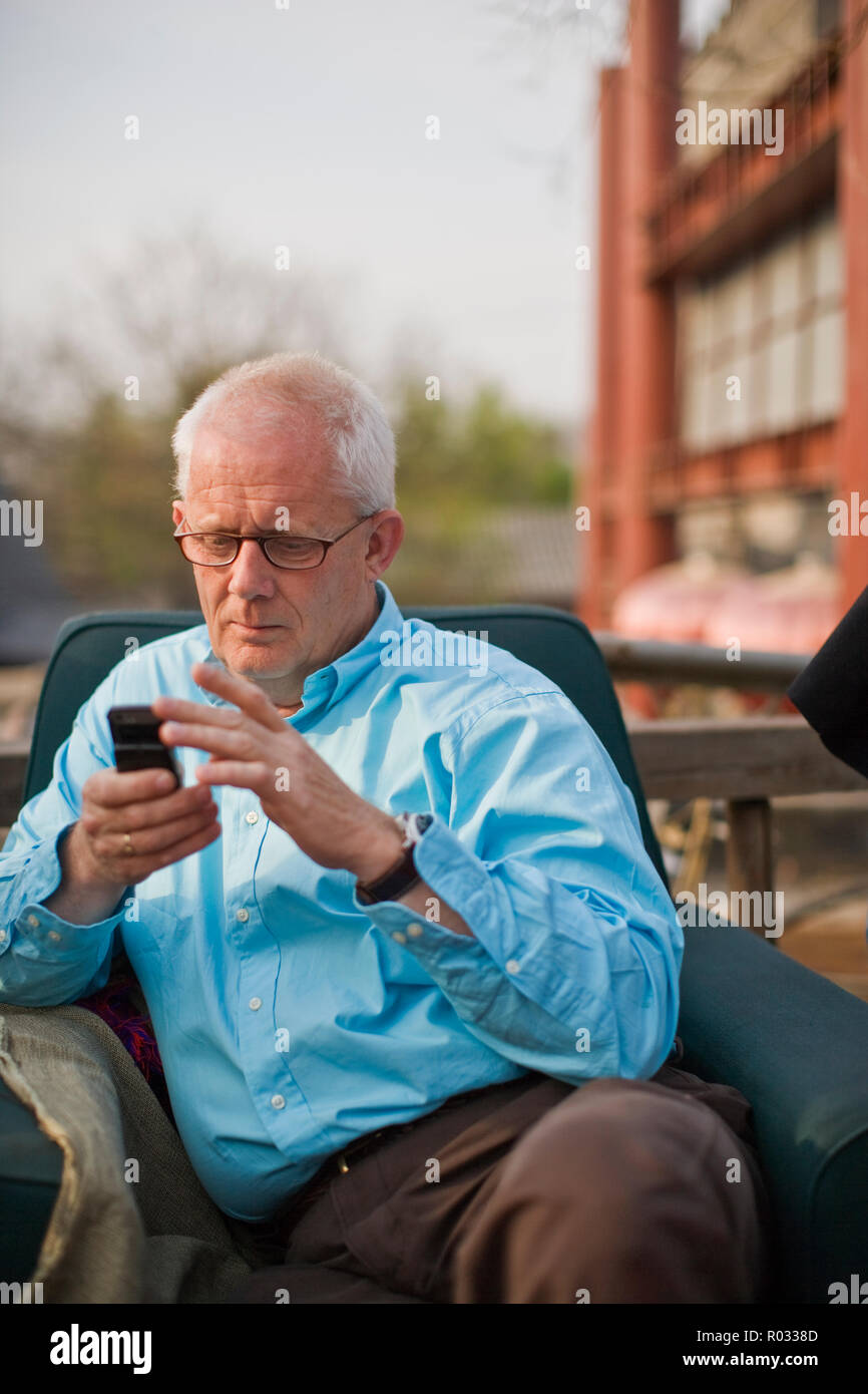 Uomo di inviare un messaggio di testo mentre è seduto in poltrona. Foto Stock