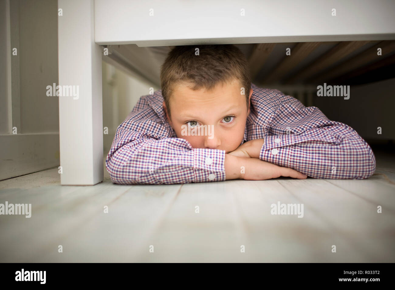 Ritratto di un ragazzo disteso sul suo stomaco mentre si nasconde sotto un letto in legno. Foto Stock