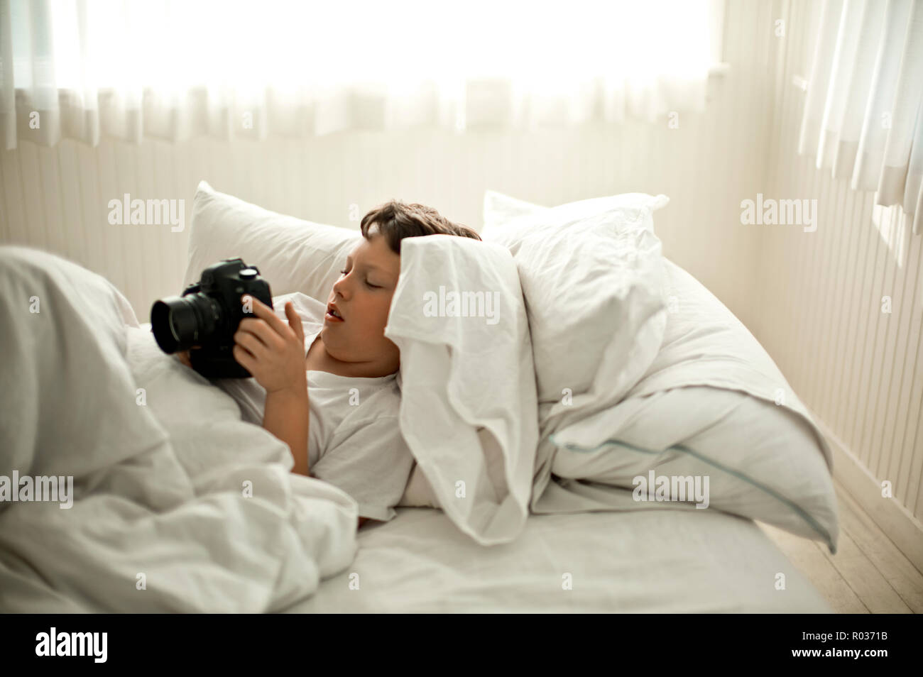 Preteen boy si trova nella camera da letto bianco giocando con una telecamera. Foto Stock