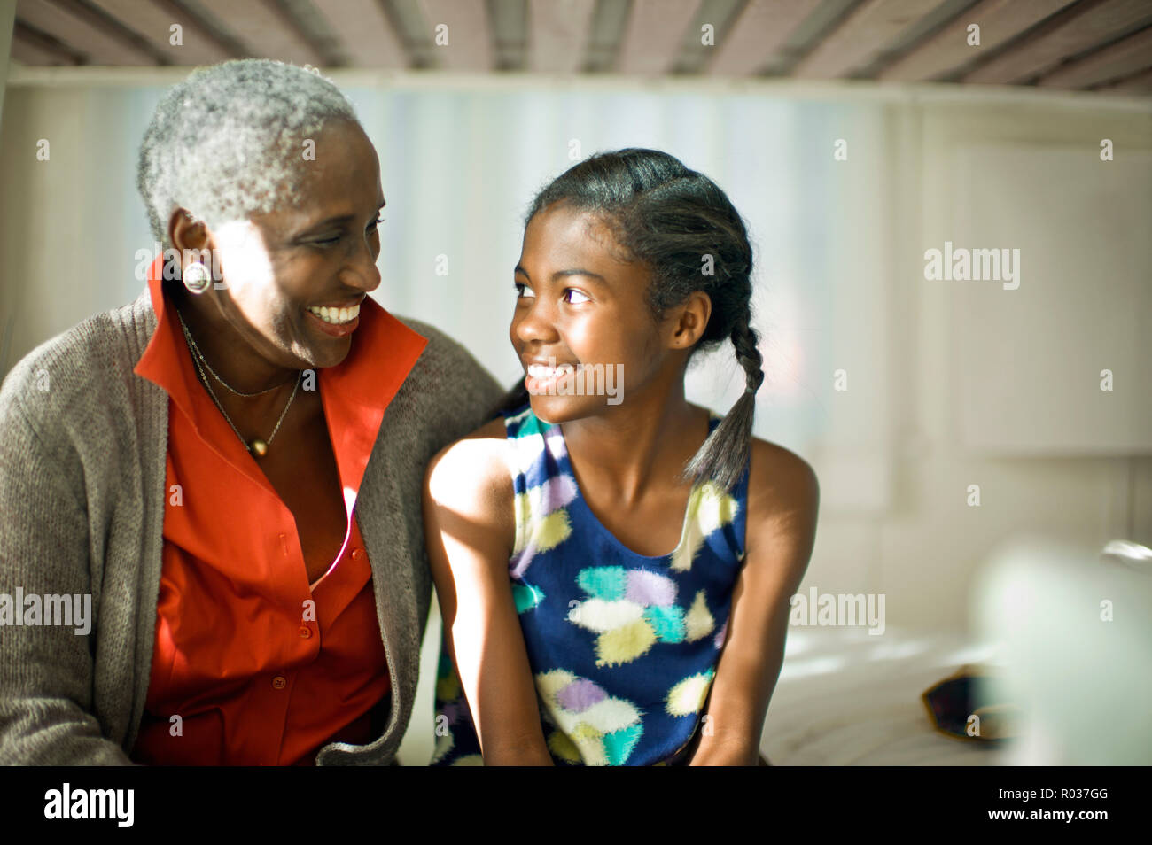 Nonna sorridente e giovane nipote seduti fianco a fianco su un letto. Foto Stock