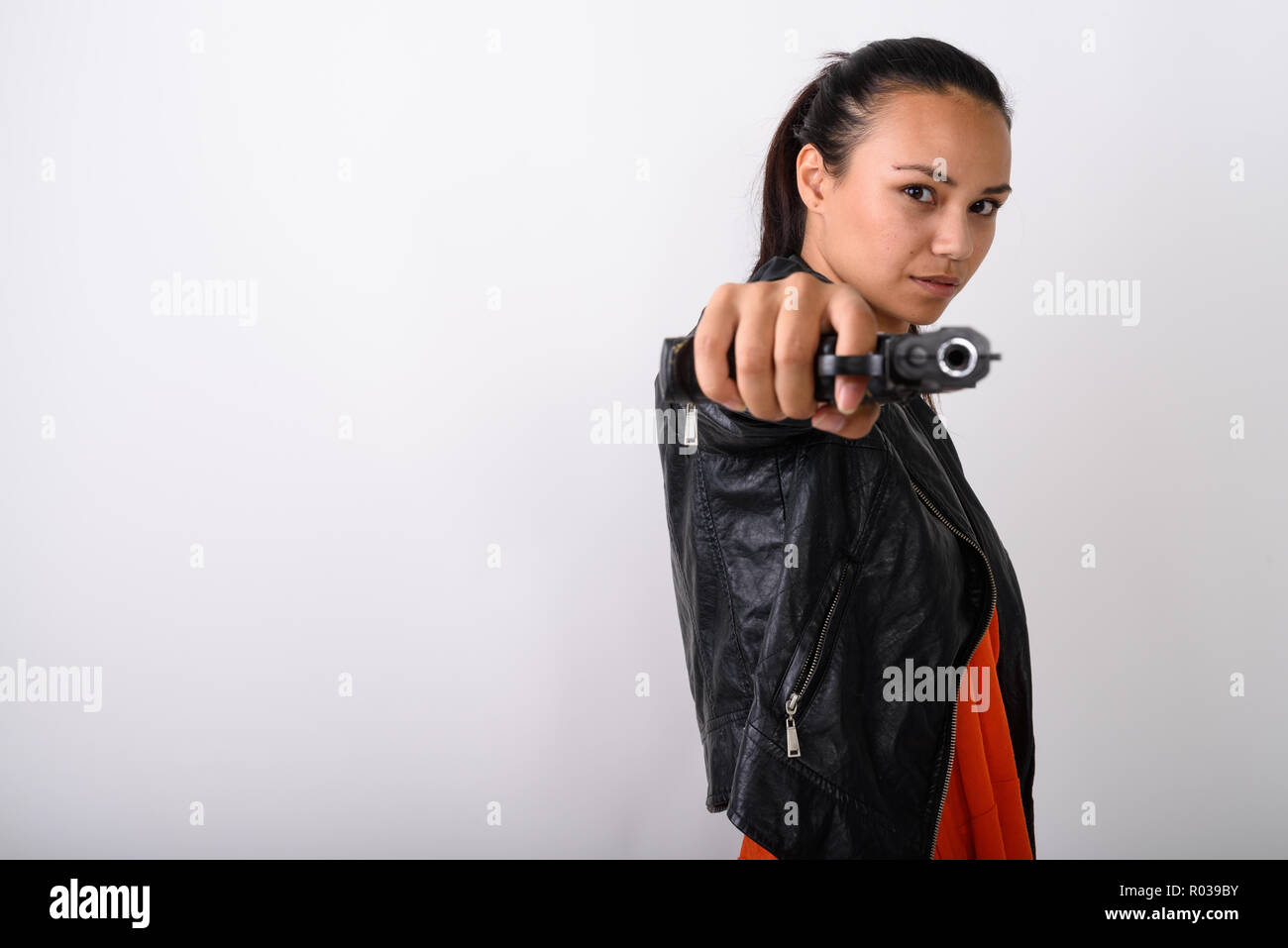 Studio shot della giovane donna asiatica pistola di puntamento in telecamera contro Foto Stock