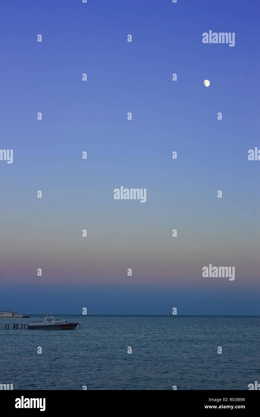 Notte al mare. La luna nel cielo senza nuvole illuminando barche a motore nei pressi di un molo Foto Stock