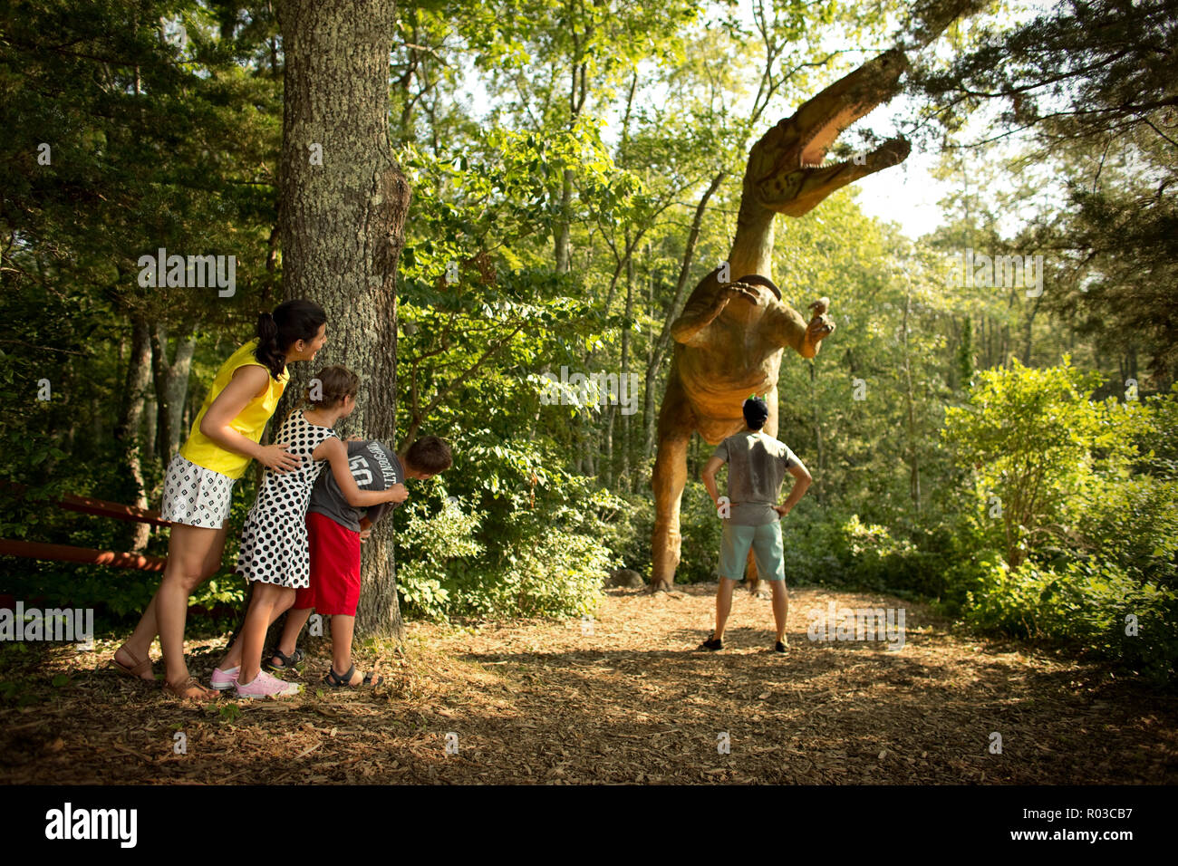 La famiglia felice scherzosamente nascondendo da una statua di un dinosauro. Foto Stock