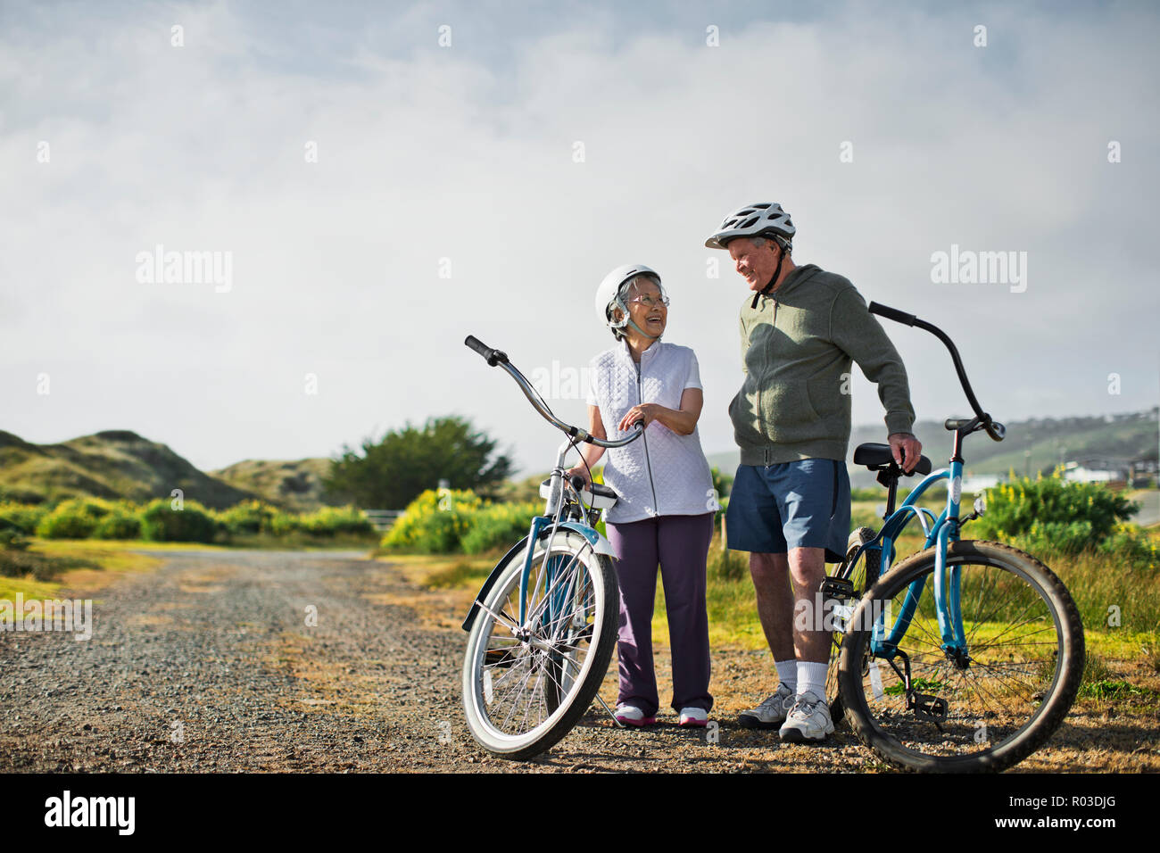 Felice coppia di anziani chat assieme come si prendono una pausa dai percorsi in bicicletta lungo una strada di campagna. Foto Stock