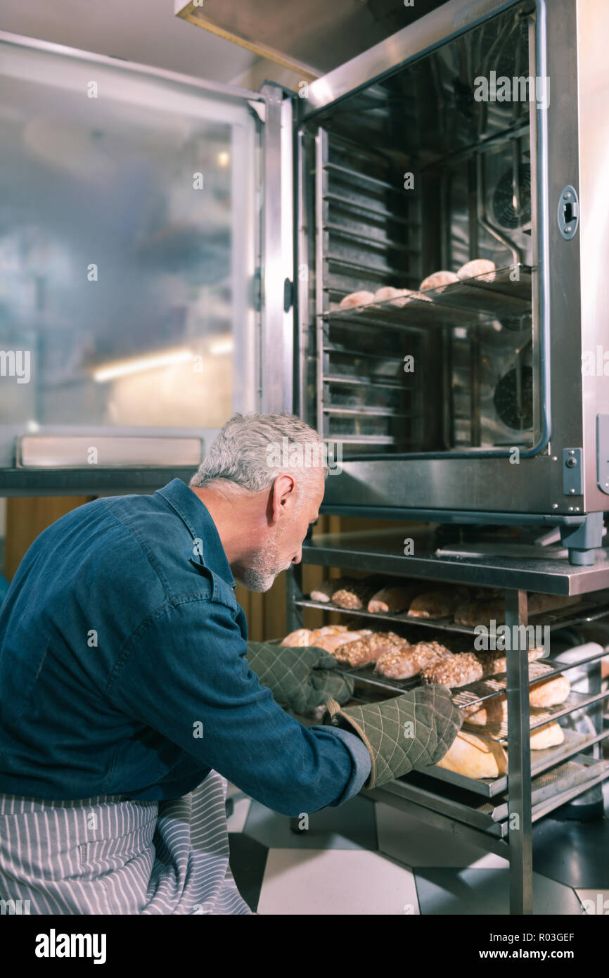 Proprietario del panificio mettendo i croissant in forno a lavorare al mattino Foto Stock