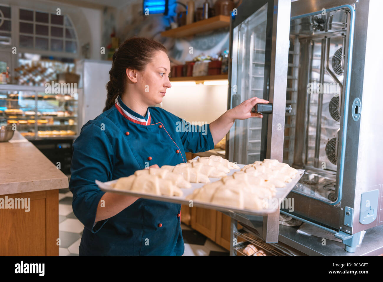 Il panettiere francese indossando giacca blu mettendo i croissant in forno Foto Stock