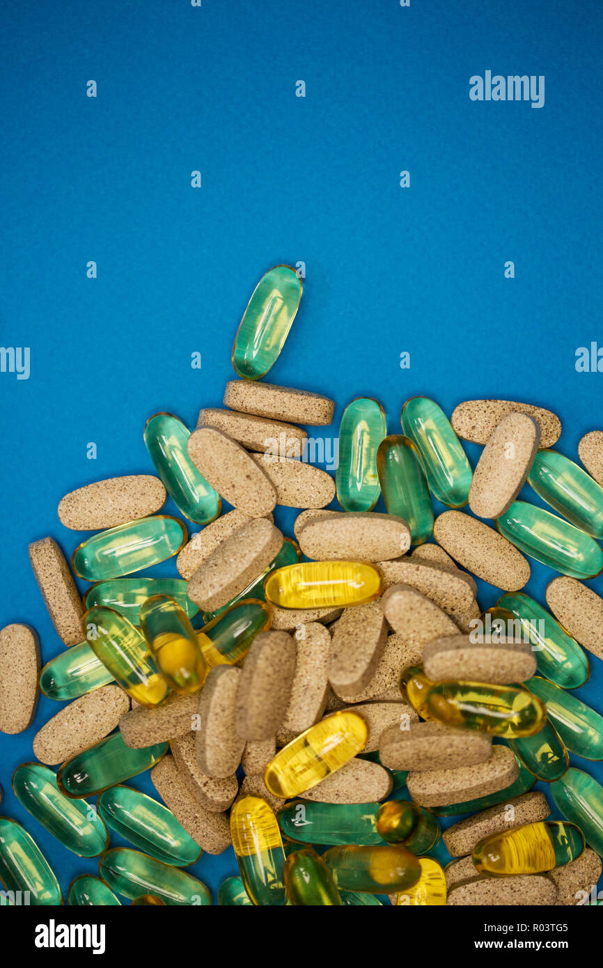 Giallo trasparente pillole e farmaci grigi sparsi su sfondo blu. Olio di pesce e vitamine Foto Stock