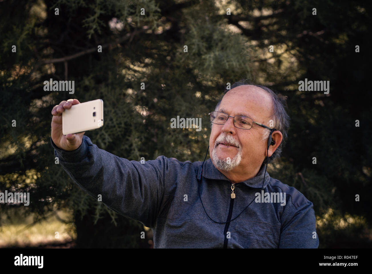 Senior uomo prendendo un selfie con smart telefono cellulare in un parco Foto Stock