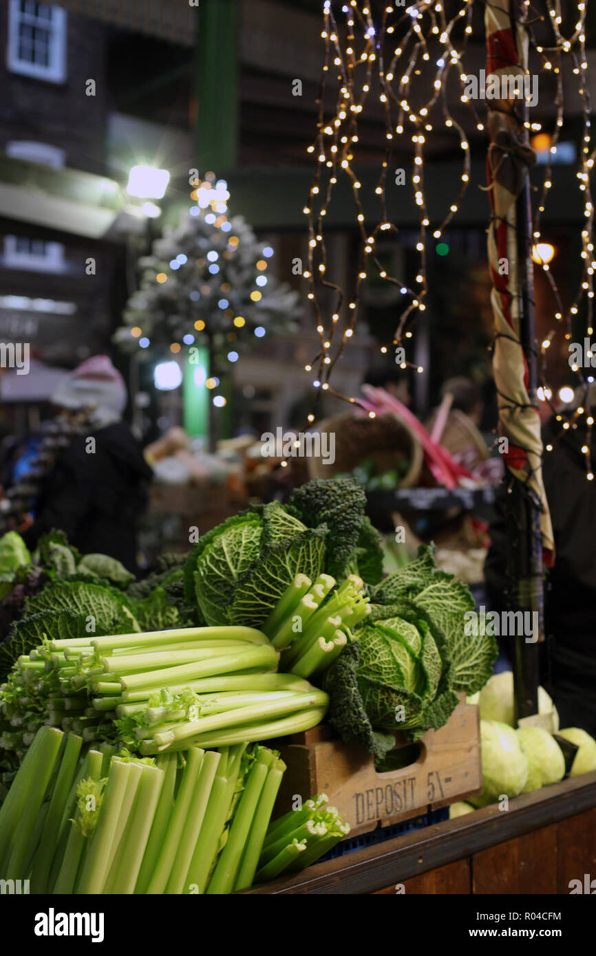 Close up di vibranti di sedano verde e savoy cavoli cappucci su un mercato con stallo al di fuori della messa a fuoco le luci di Natale in background Foto Stock
