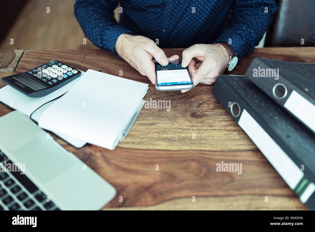 Uomo seduto al tavolo per ufficio SMS sullo smartphone Foto Stock