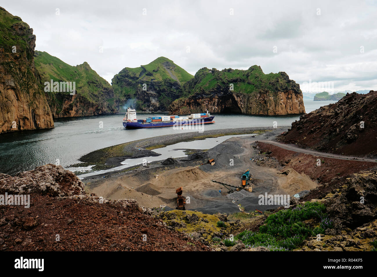 Una nave da carico la navigazione le strette e canale impressionante entrata in l'isola vulcanica di Heimaey in Vestmannaeyjar Islanda. Foto Stock