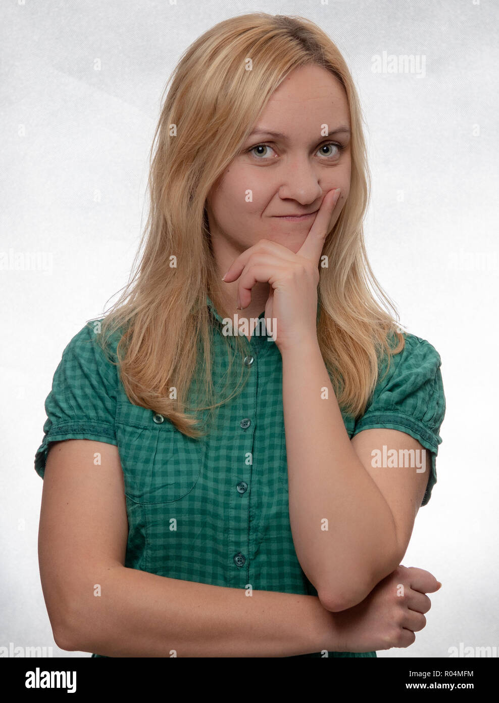 Curioso giovane donna casual in camicia verde guardando dritto nella telecamera Foto Stock