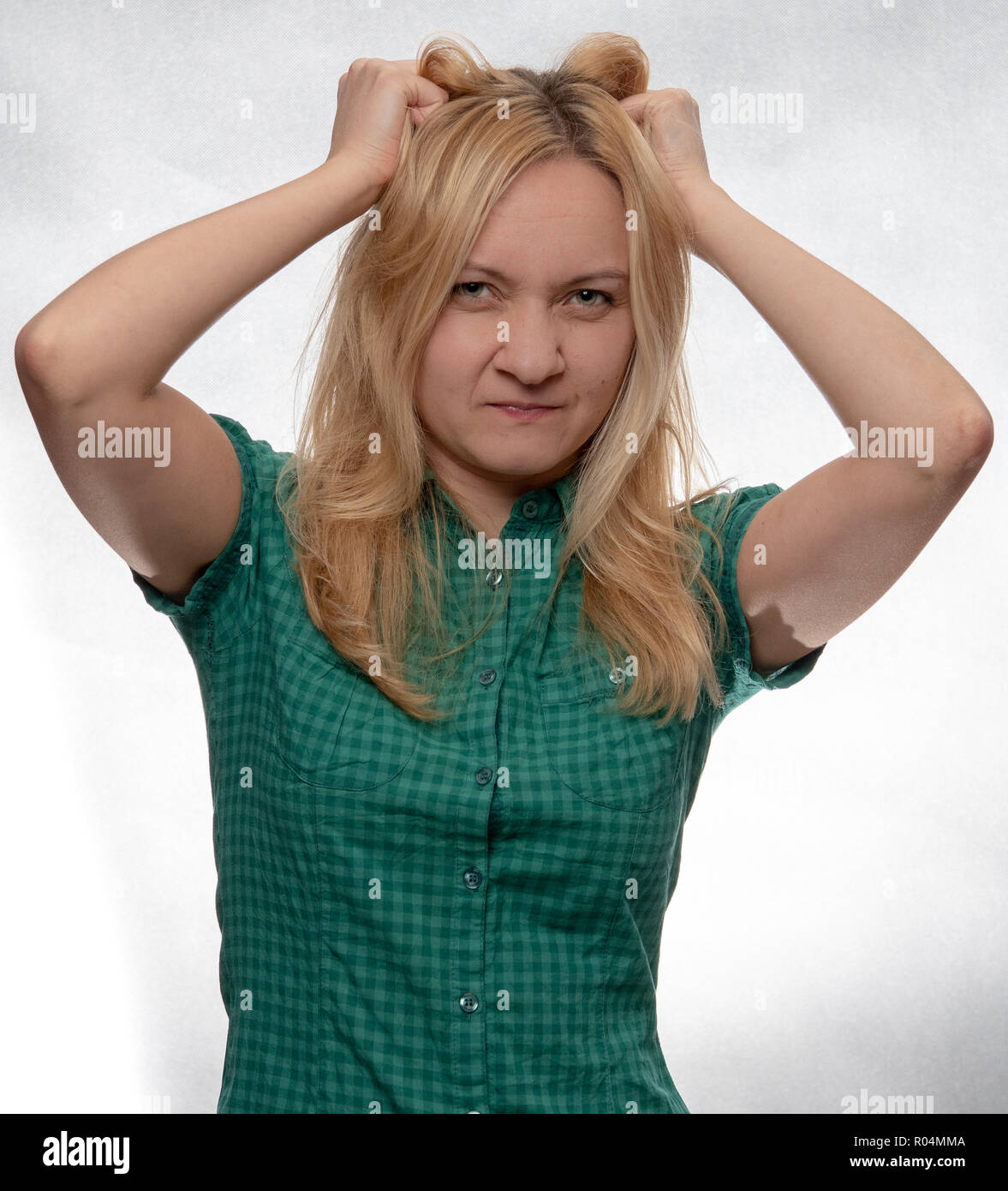 Arrabbiato giovane donna casual in camicia verde con le mani nei capelli guardando dritto nella telecamera Foto Stock