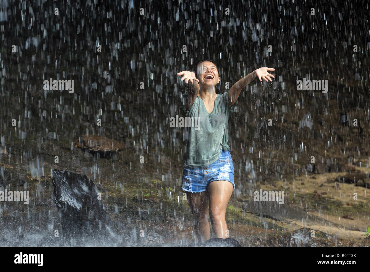 Donna felice godendo di acqua che cade dalla cascata tropicale, Thailandia Foto Stock