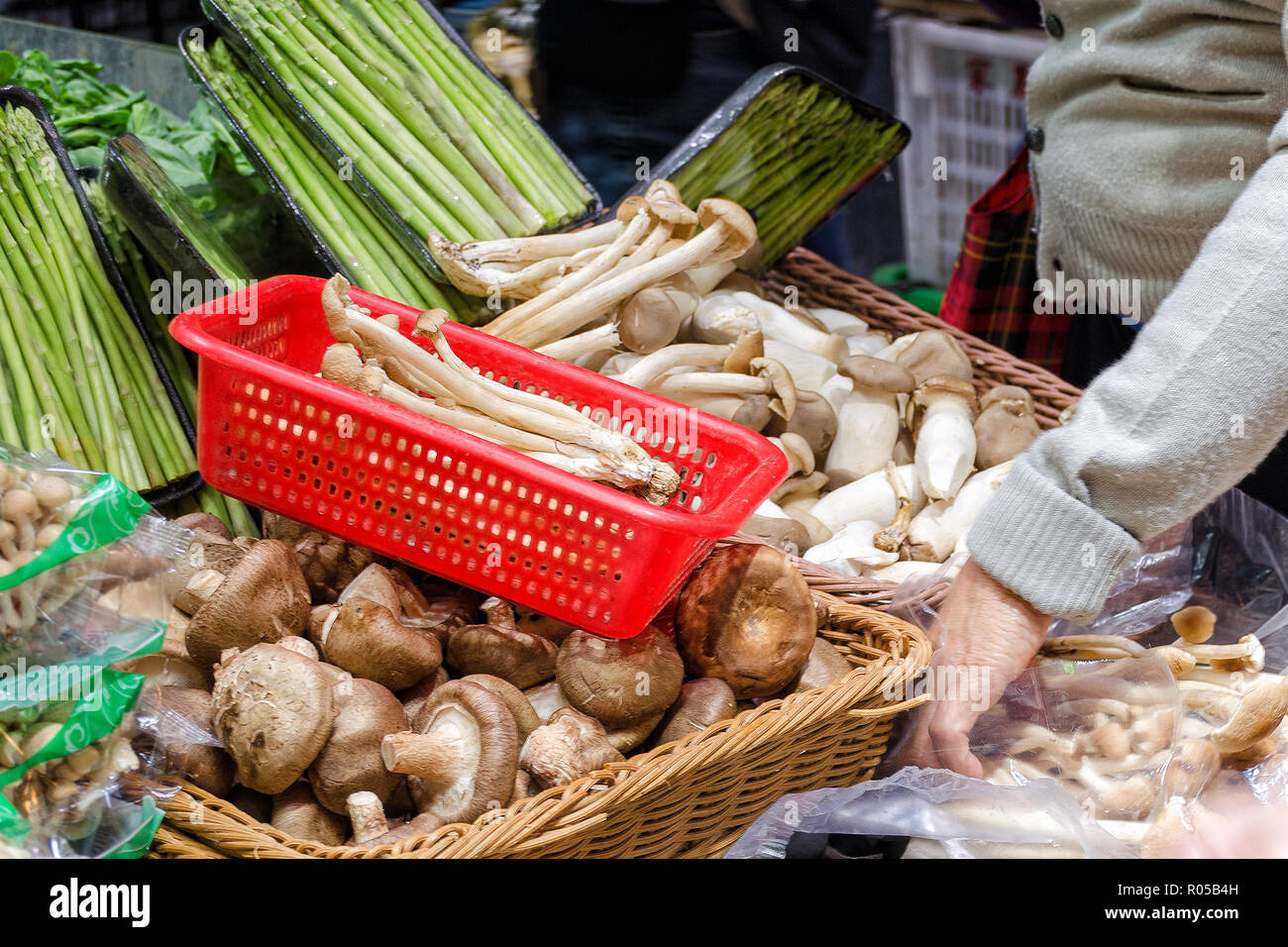 Stallo con funghi e asparagi germogli, mano riempie il cestello con i funghi. Foto con la sfocatura in movimento. Hong Kong, Cina. Foto Stock