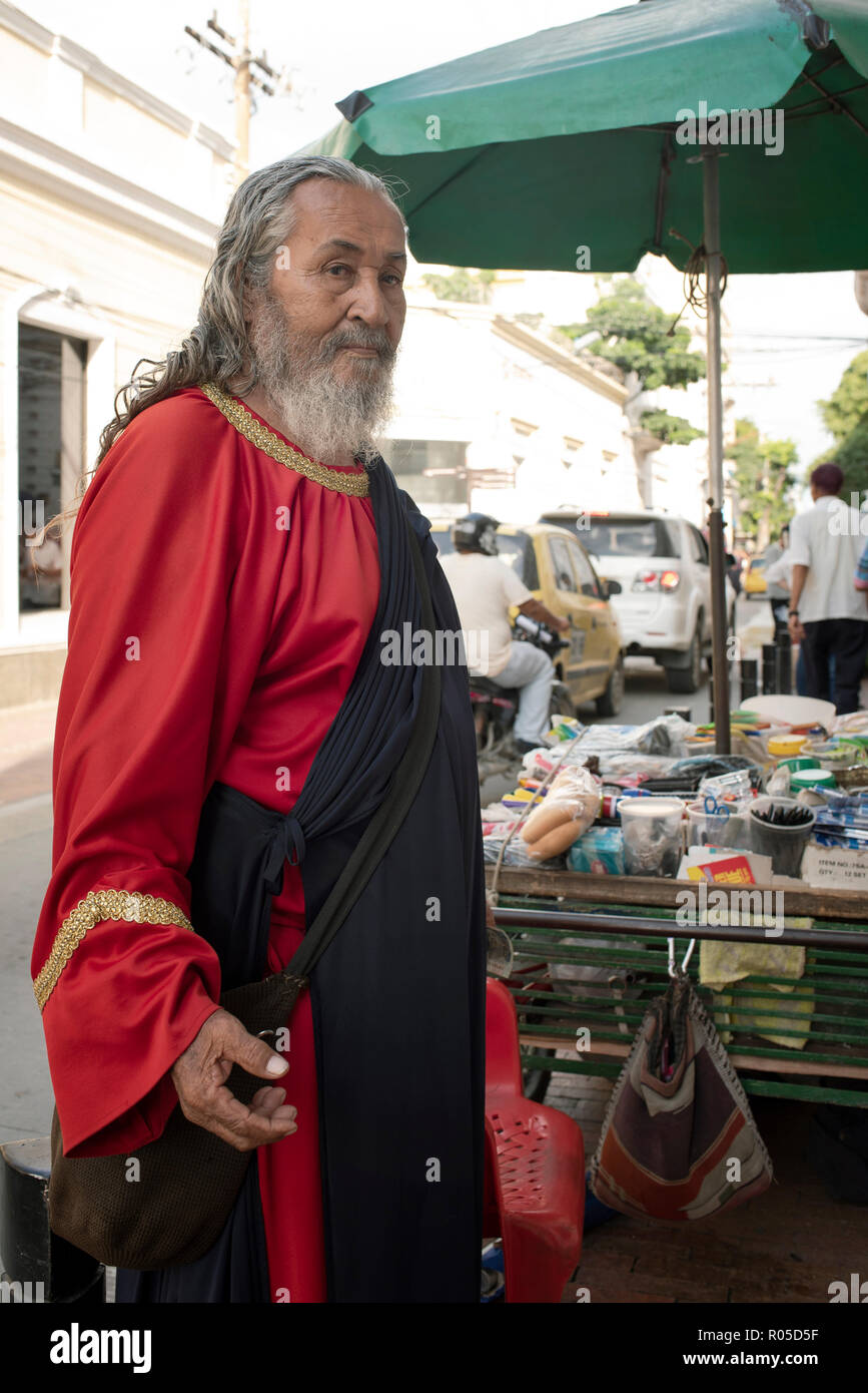 Colombiano di vecchio uomo vestito stile medievale e la vendita di prodotti di consumo quotidiano dal suo carrello nel centro cittadino di Santa Marta, Colombia. Sep 2018 Foto Stock