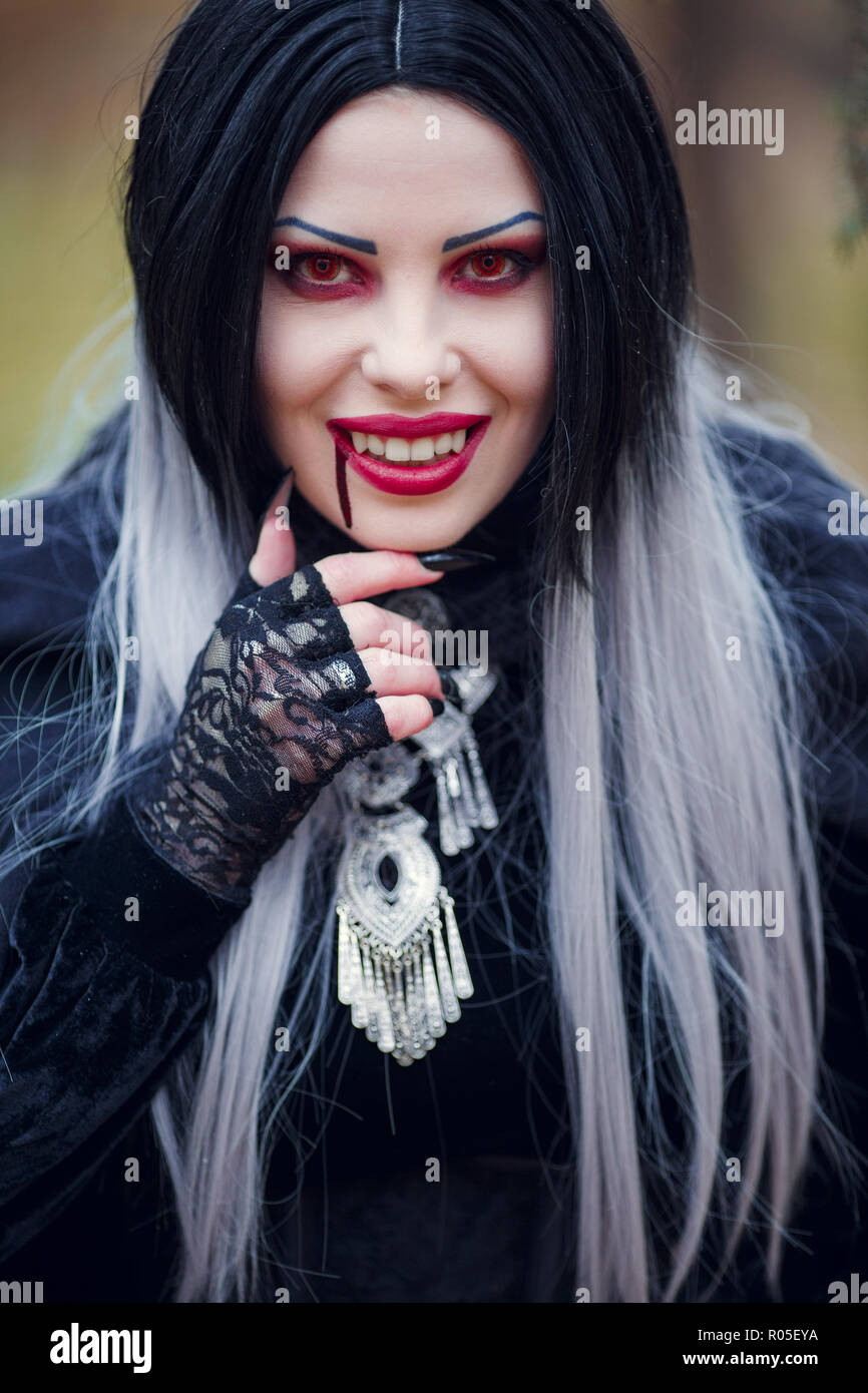 Immagine del vampiro sorridente donna con flusso di sangue in prossimità della bocca, occhi rossi su sfondo sfocato Foto Stock