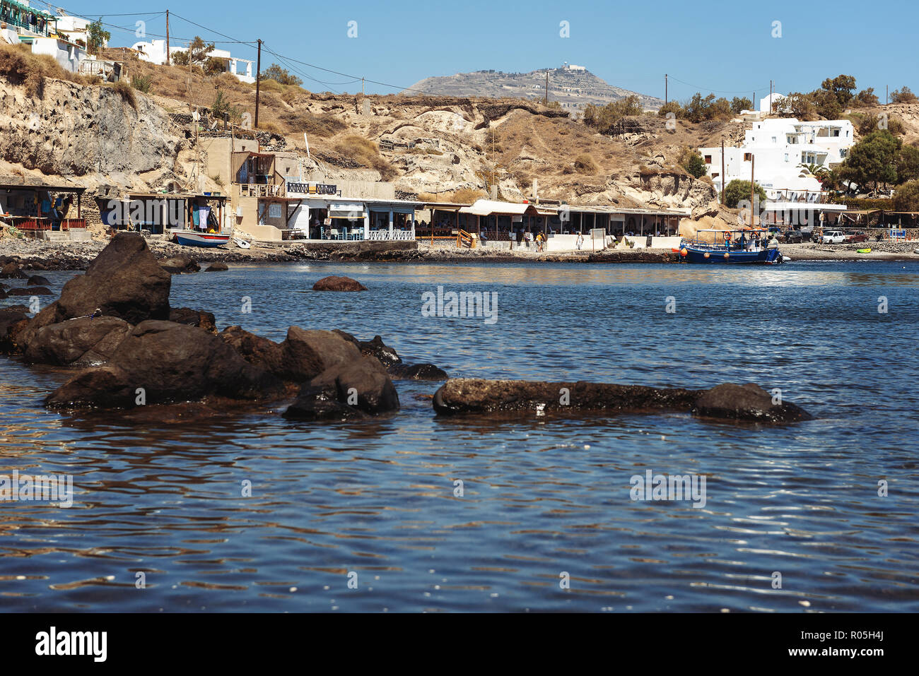 SANTORINI, Grecia - Agosto 2018: costa rocciosa di Isola con piccole taverne in prossimità di acqua Foto Stock