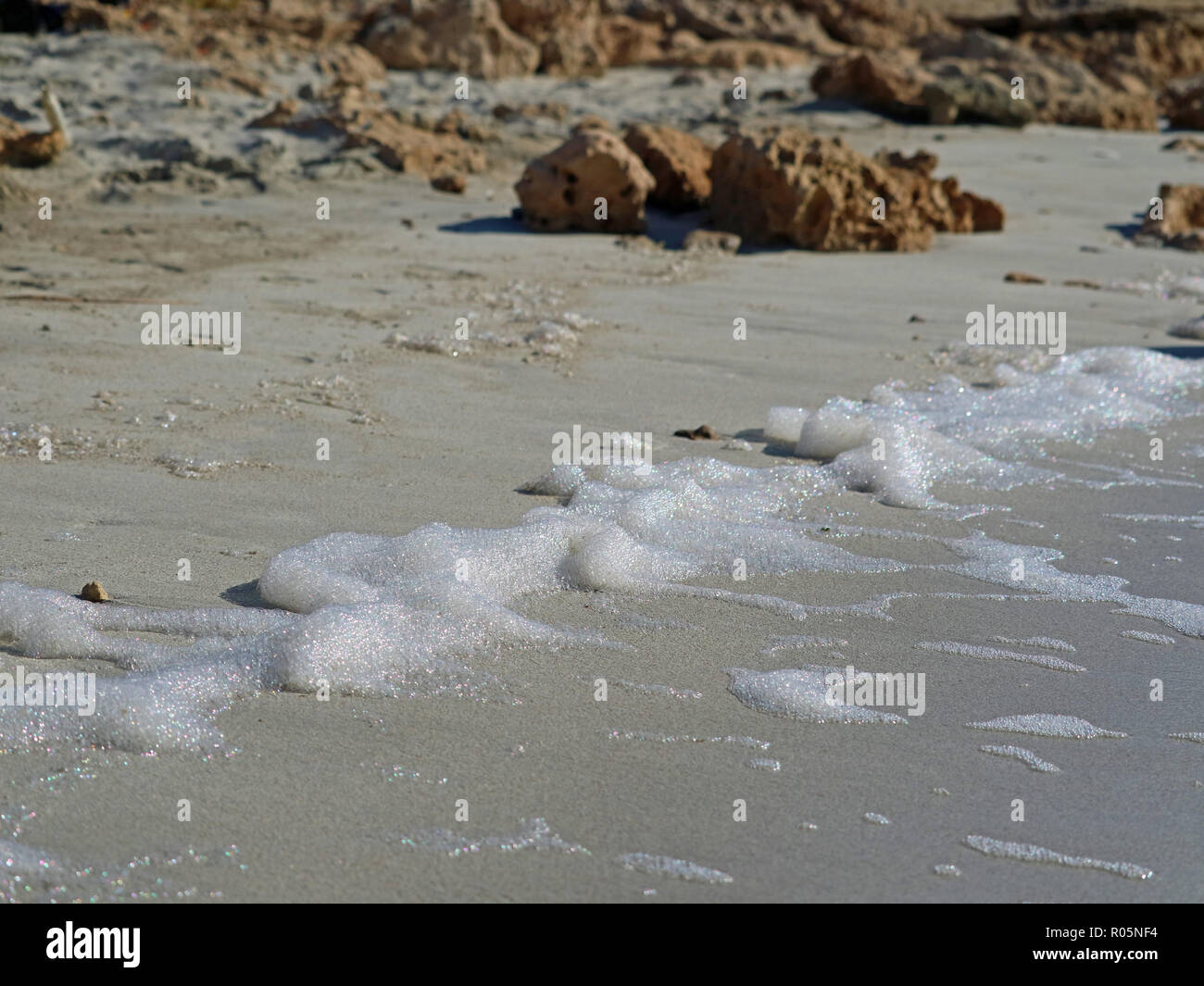 Close up di bolle delle onde del mare sulla spiaggia con sabbia e pietre su sfondo Foto Stock