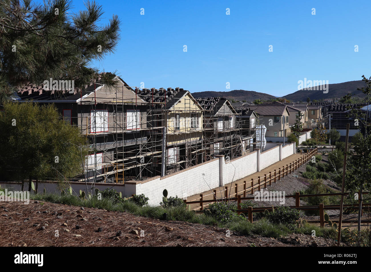 Quattro nuove case di famiglia in costruzione e circondato da impalcature in una zona suburbana con sentieri pubblici, scherma, copia dello spazio nel cielo blu Foto Stock