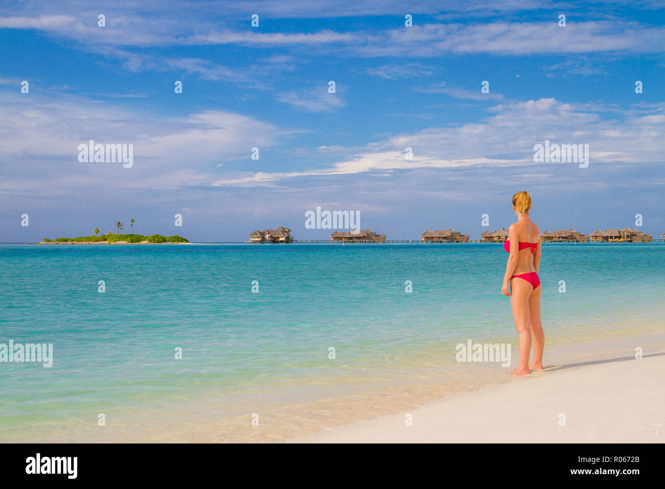 Moda donna sulla spiaggia in rosa bikini, vista su acqua di lusso ville in Maldive. Tranquilla spiaggia tropicale paesaggistico, blu del mare e la sabbia bianca Foto Stock