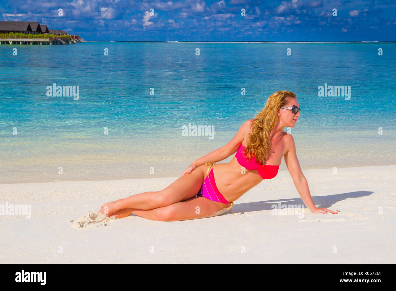 Ritratto di sorridente giovane donna posa sulla spiaggia e guardando lontano in rosa bikini e occhiali da sole. Spiaggia esotica con copia spazio, donne attraenti gode Foto Stock