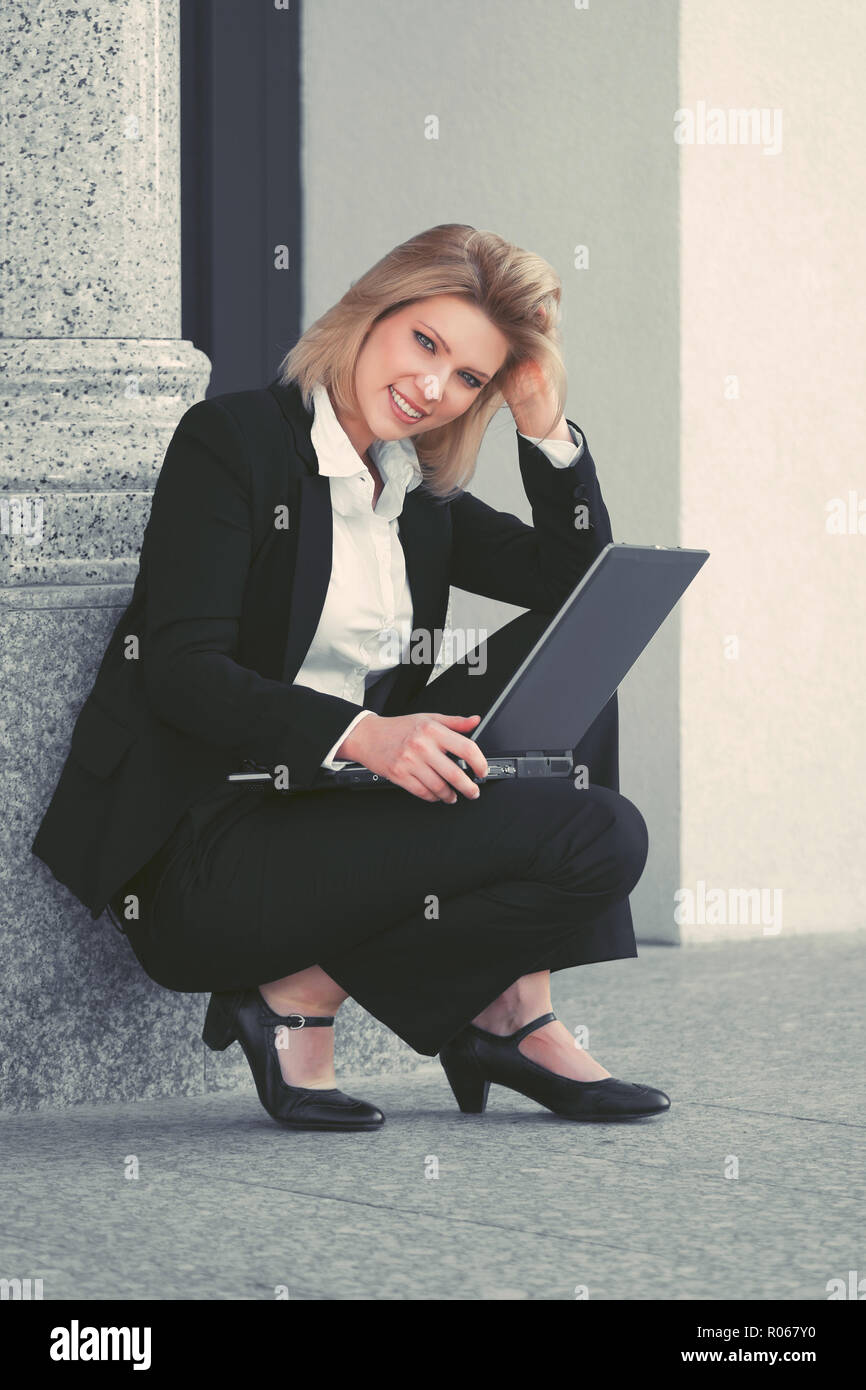 Giovane imprenditrice utilizzando computer portatile presso la sede di un ufficio. Elegante modello di moda in abito nero Foto Stock