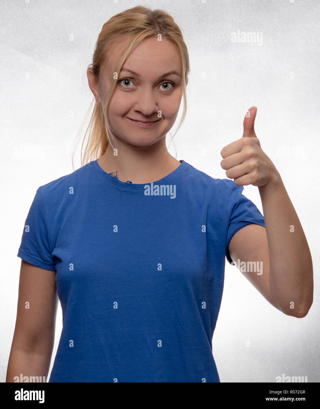 Felice giovane donna con il pollice in alto nel casual maglietta blu Foto Stock