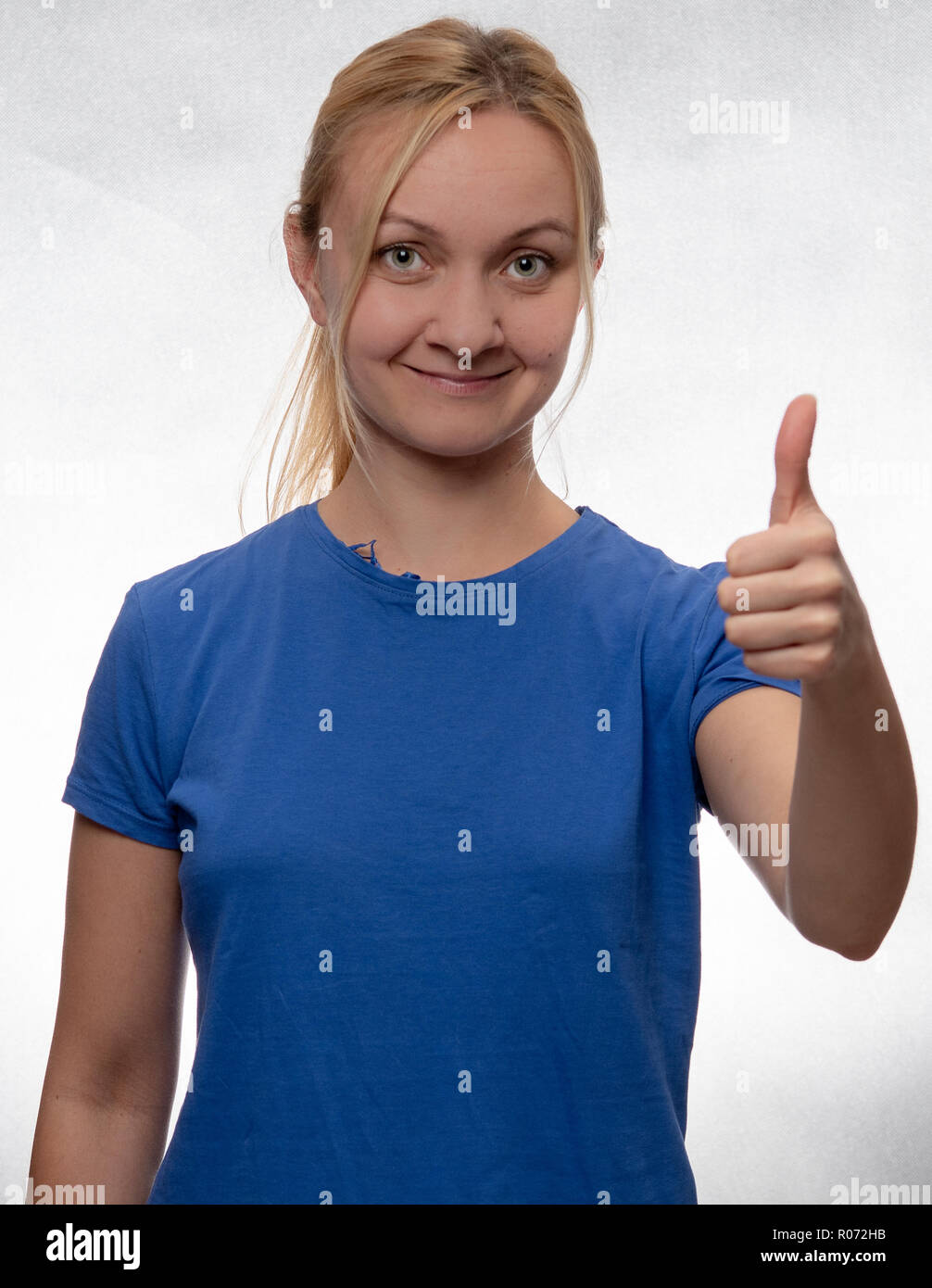Felice giovane donna con il pollice in alto nel casual maglietta blu Foto Stock
