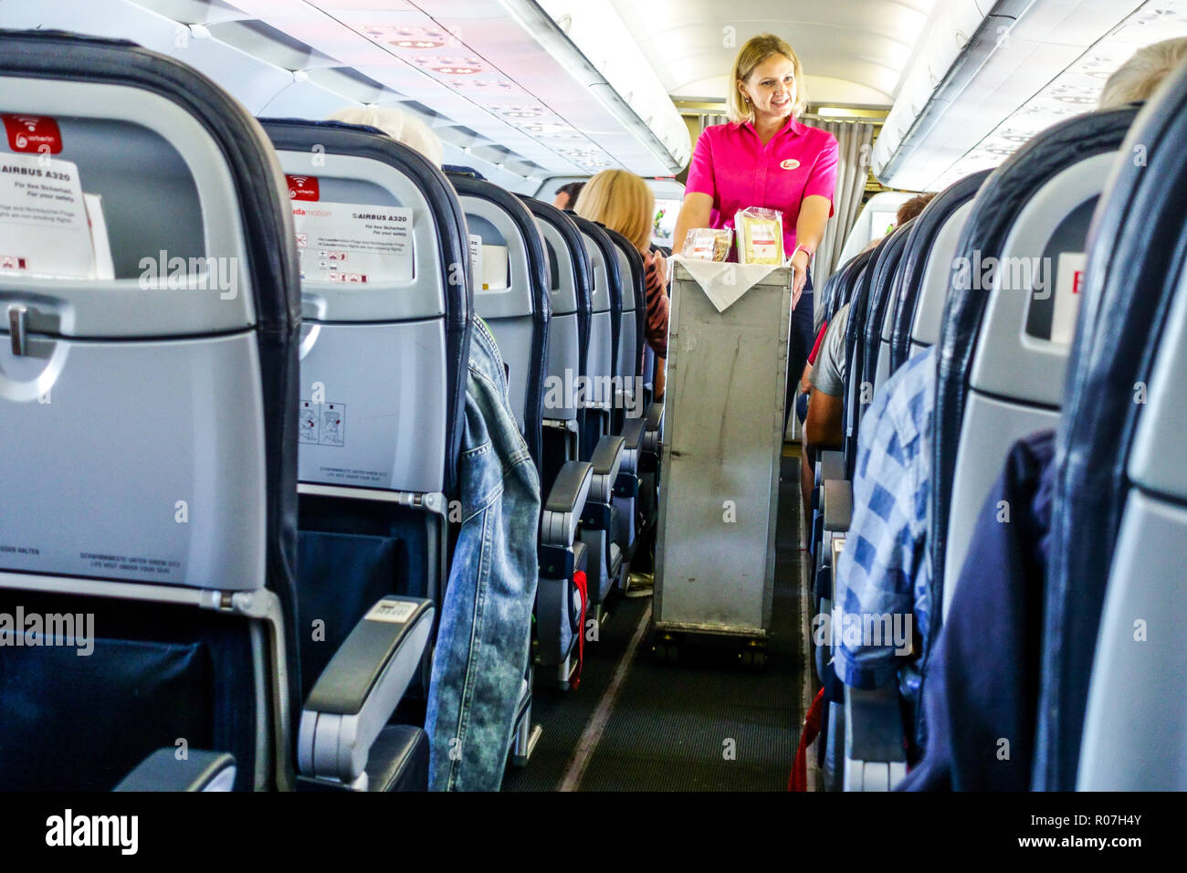 A bordo di Laudamotion Airbus A320, una hostess in una stretta corsia tra i posti offre le merci dai posti dell'aereo del trolley Foto Stock