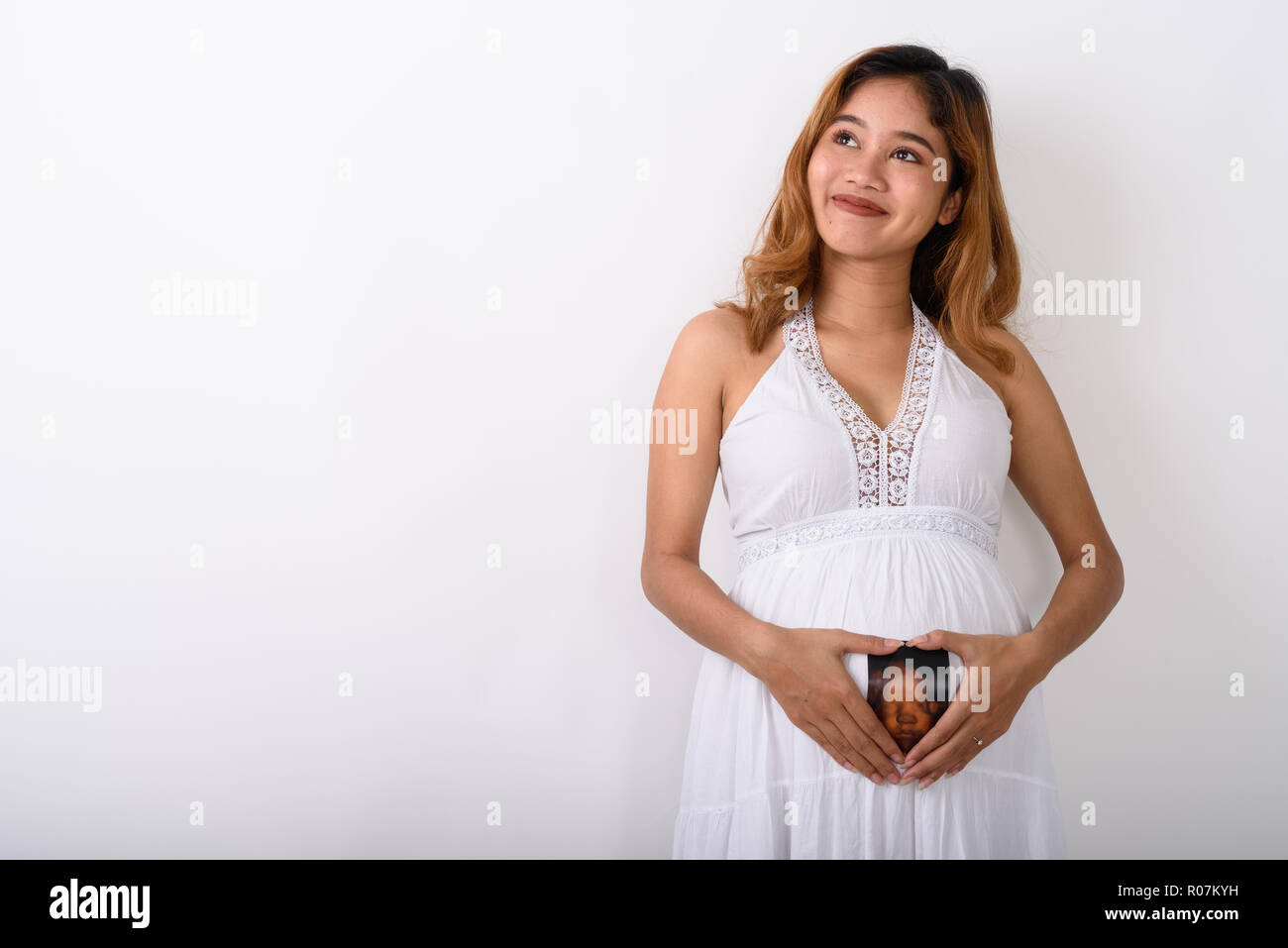 Studio shot di giovani asiatici donna incinta pensando mentre facendo Foto Stock