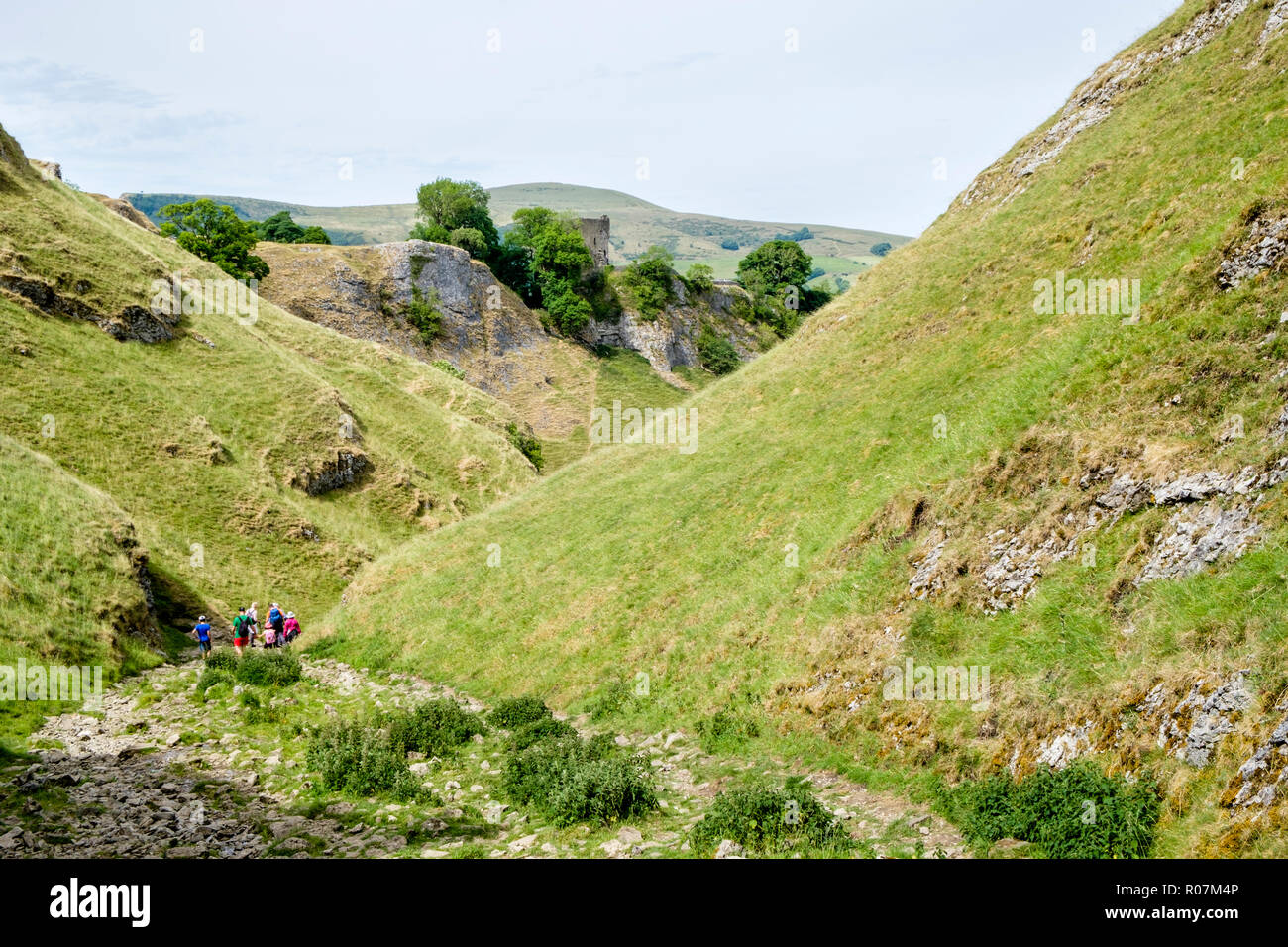 Walkers scendendo il Sentiero pietroso di calcare modo in grotta Dale, con: Peveril Castle in distanza, Derbyshire, Peak District, England, Regno Unito Foto Stock