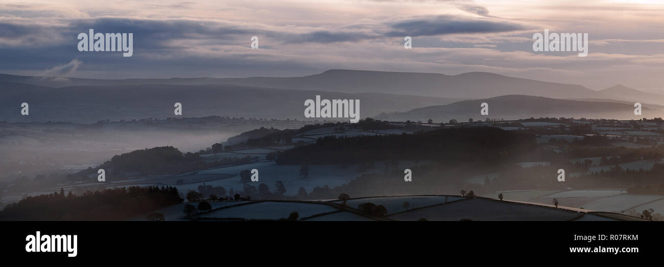 Una vista panoramica della nebbia salendo attraverso farmalnd all'alba, Brecon Beacons, Ottobre 2018 Foto Stock