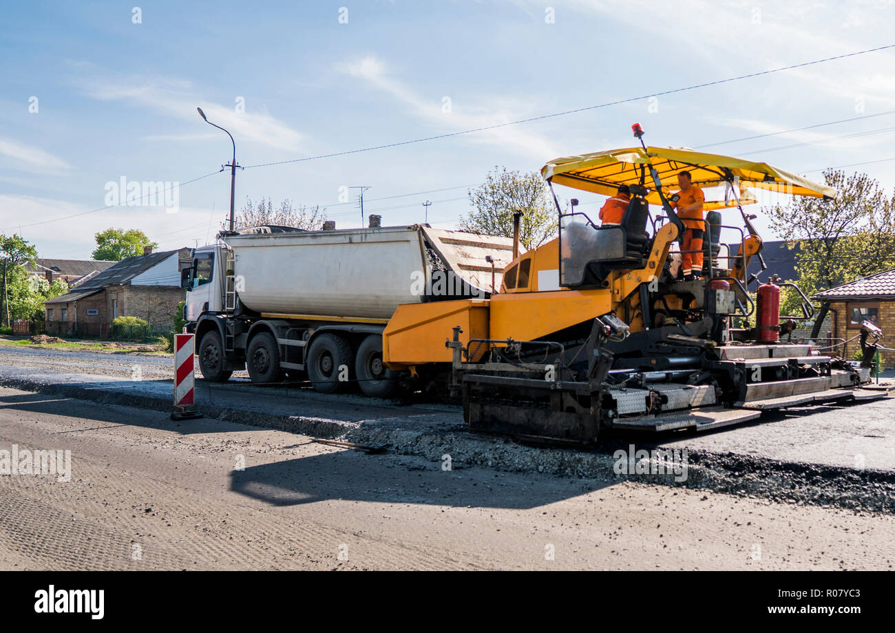 Lavoratore di asfalto operativo lastricatore macchina durante la costruzione di strade e lavori di riparazione. Un lastricatore finisher, asfalto di finitura o macchina di pavimentazione disporre uno strato di asfalto. Ripavimentazione Foto Stock