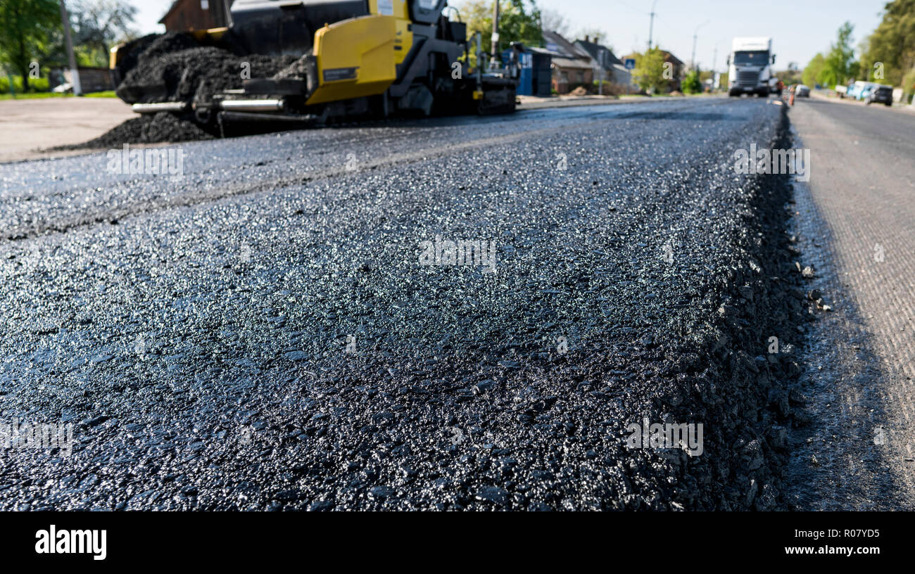 Lavoratore di asfalto operativo lastricatore macchina durante la costruzione di strade e lavori di riparazione. Un lastricatore finisher, asfalto di finitura o macchina di pavimentazione disporre uno strato di asfalto. Ripavimentazione Foto Stock