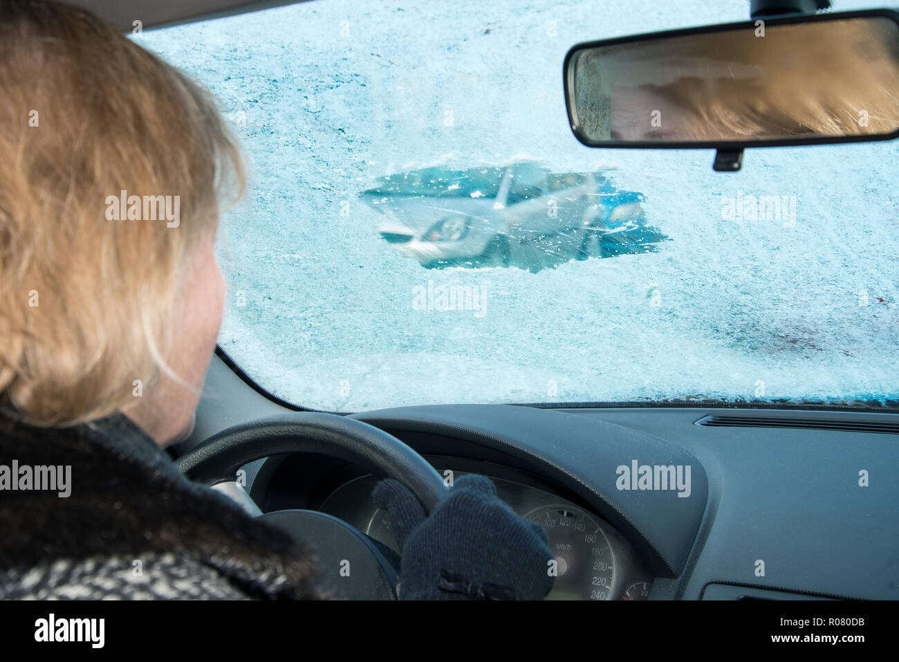 La donna è in cerca di una vettura attraverso un piccolo divario graffiato in un gelido parabrezza Foto Stock