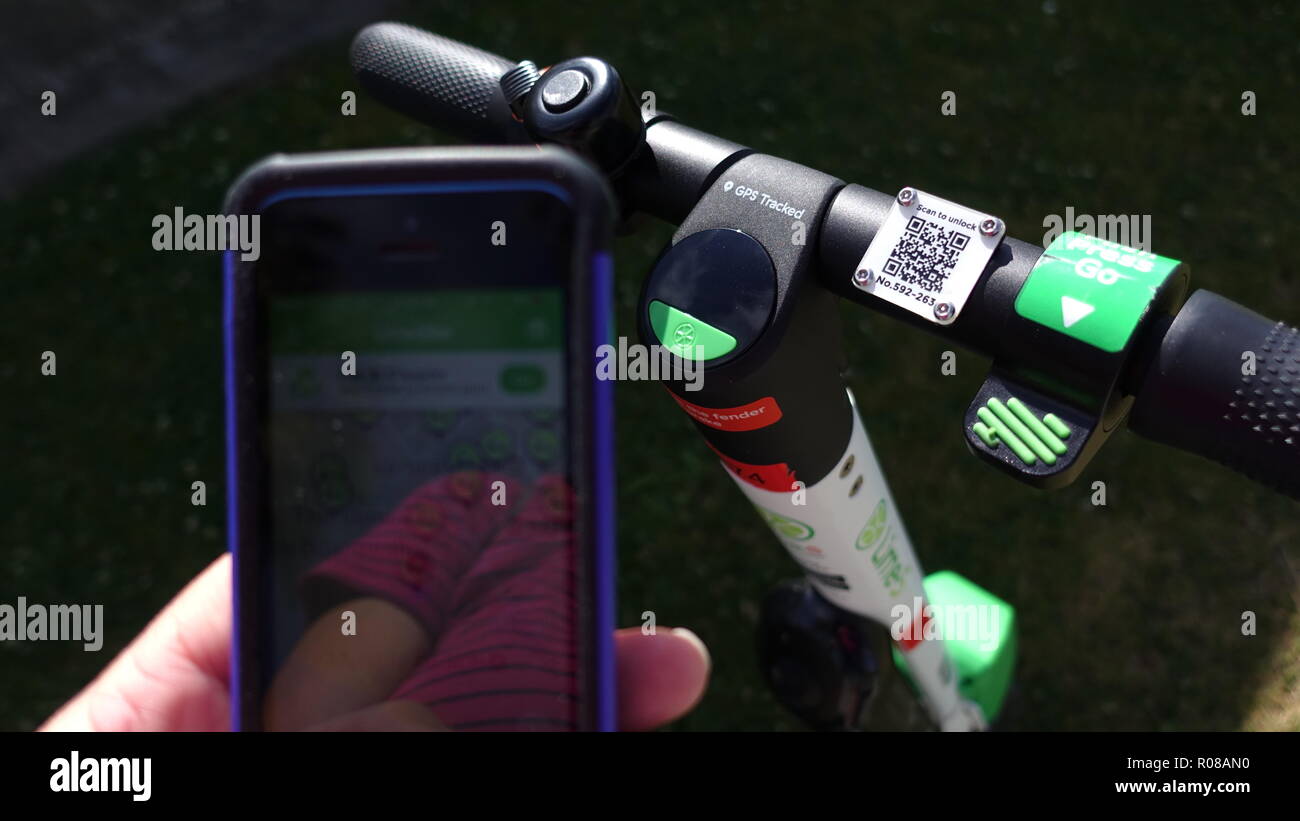 In prossimità del manubrio ed eseguire la scansione di un simbolo di calce-S scooter elettrico e la mano che tiene il telefono cellulare con calce aperte bike app Foto Stock