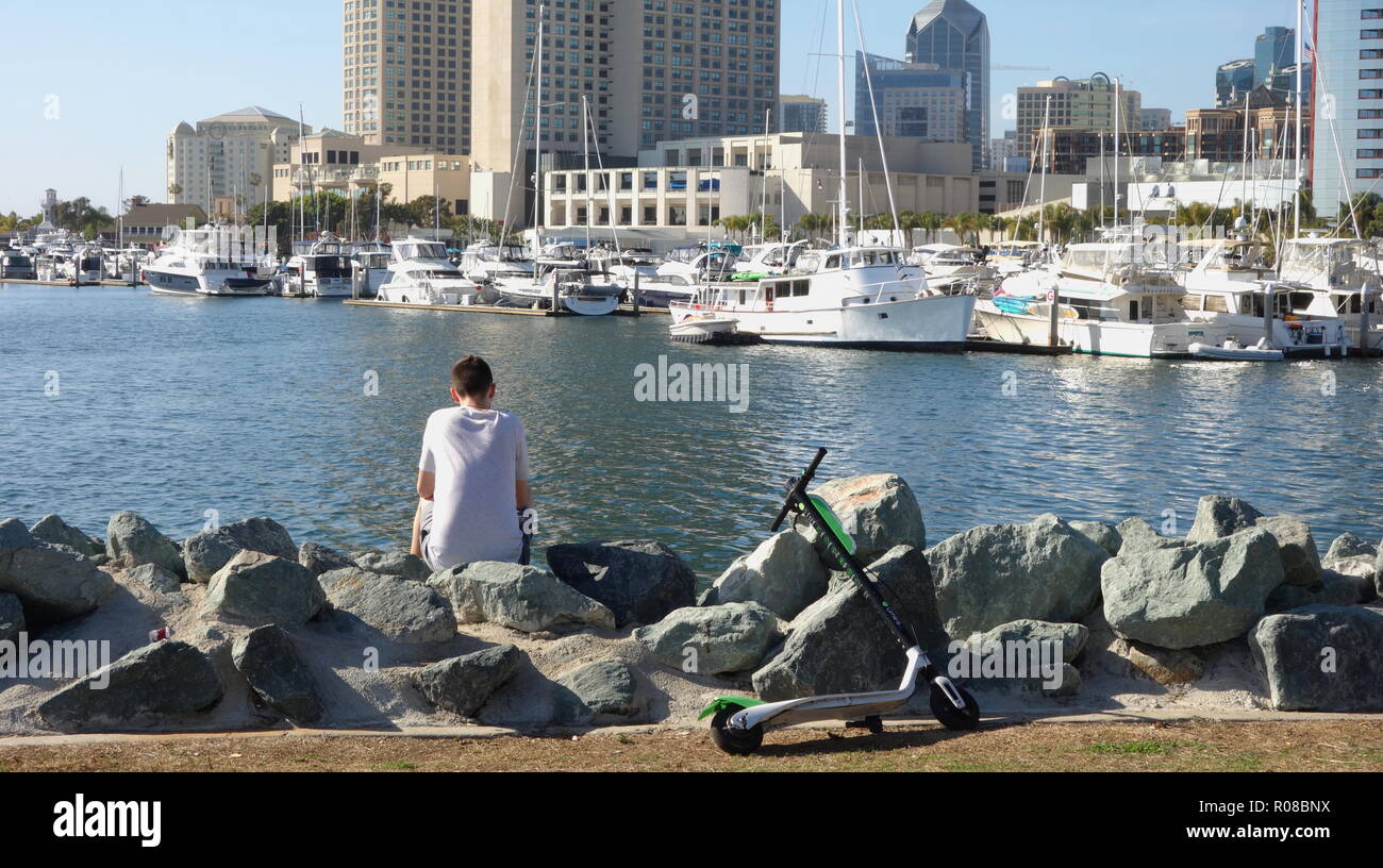 Un uomo si gode della vista del San Diego Marina, con calce-S scooter elettrico parcheggio nelle vicinanze Foto Stock