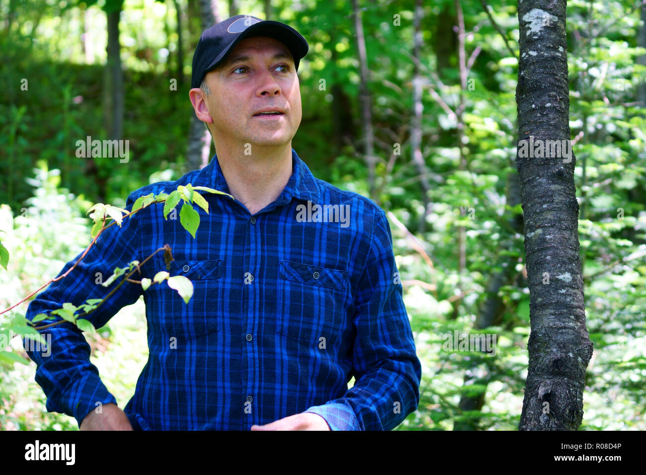 Un uomo caucasico sta cercando la telecamera per un ritratto durante le escursioni nella foresta che indossa un controllo blu T-shirt e un cappello nero. Foto Stock
