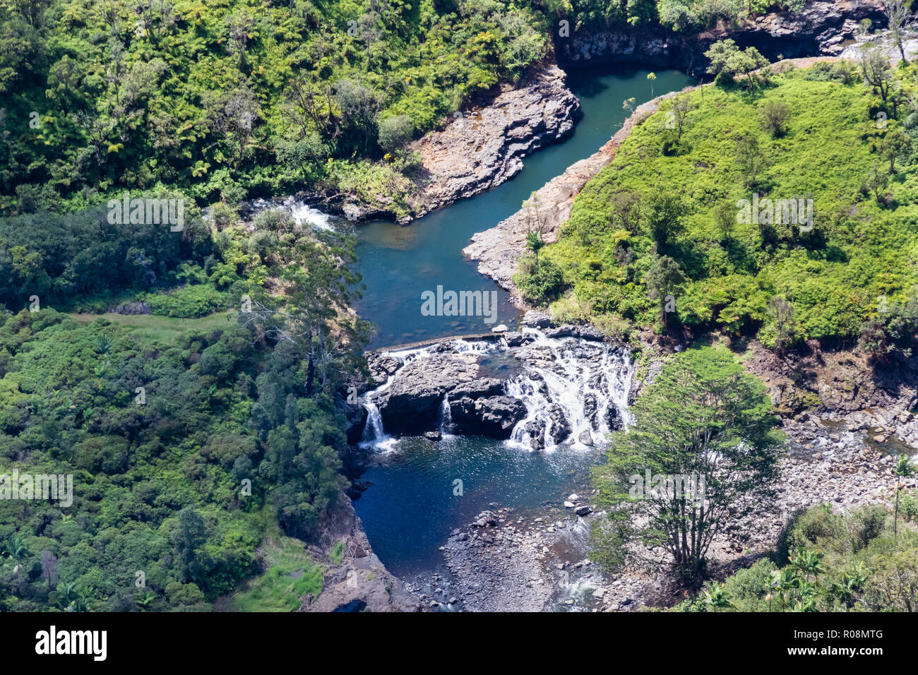 Vista aerea del flusso e cascata in prossimità di Hilo, Hawaii. Laghetto superiore cascades su roccia alla piscina inferiore. Area è circondata dalla foresta pluviale. Foto Stock