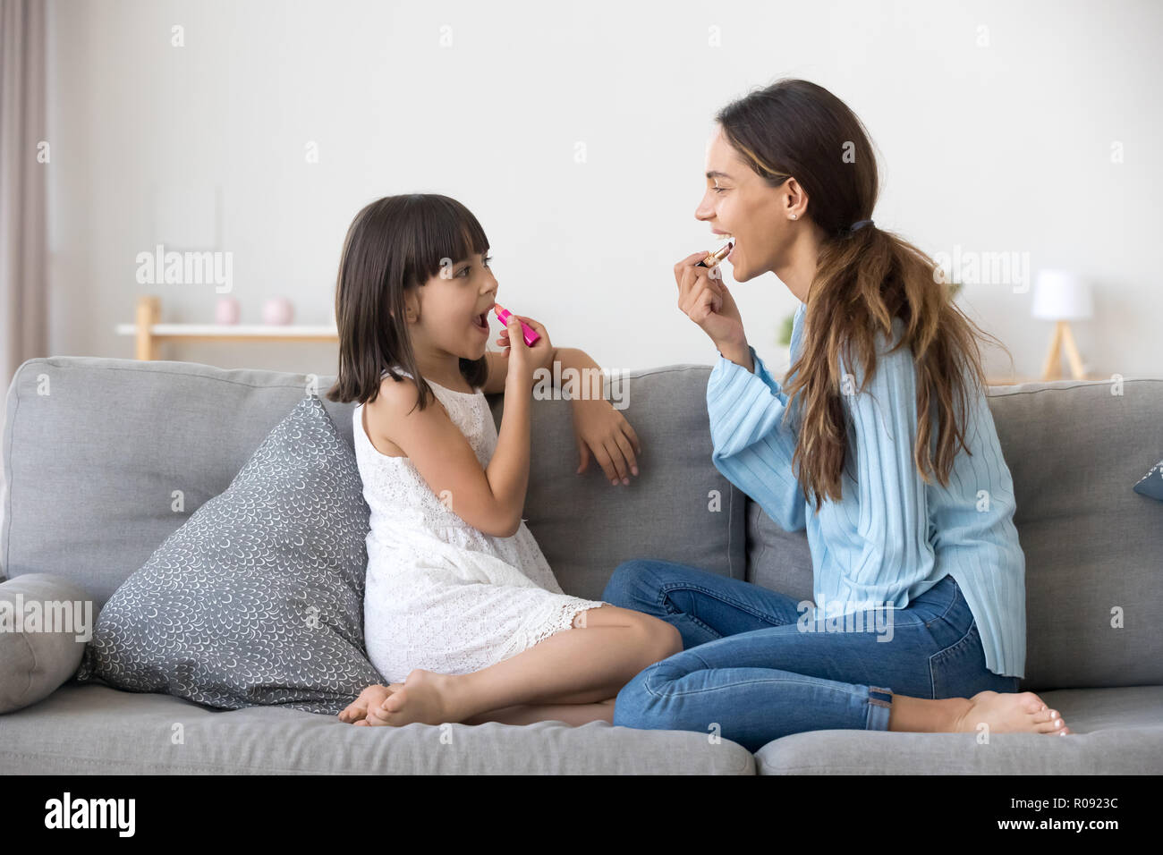 Piccola figlia divertendosi con la mamma il rossetto sulle labbra Foto Stock