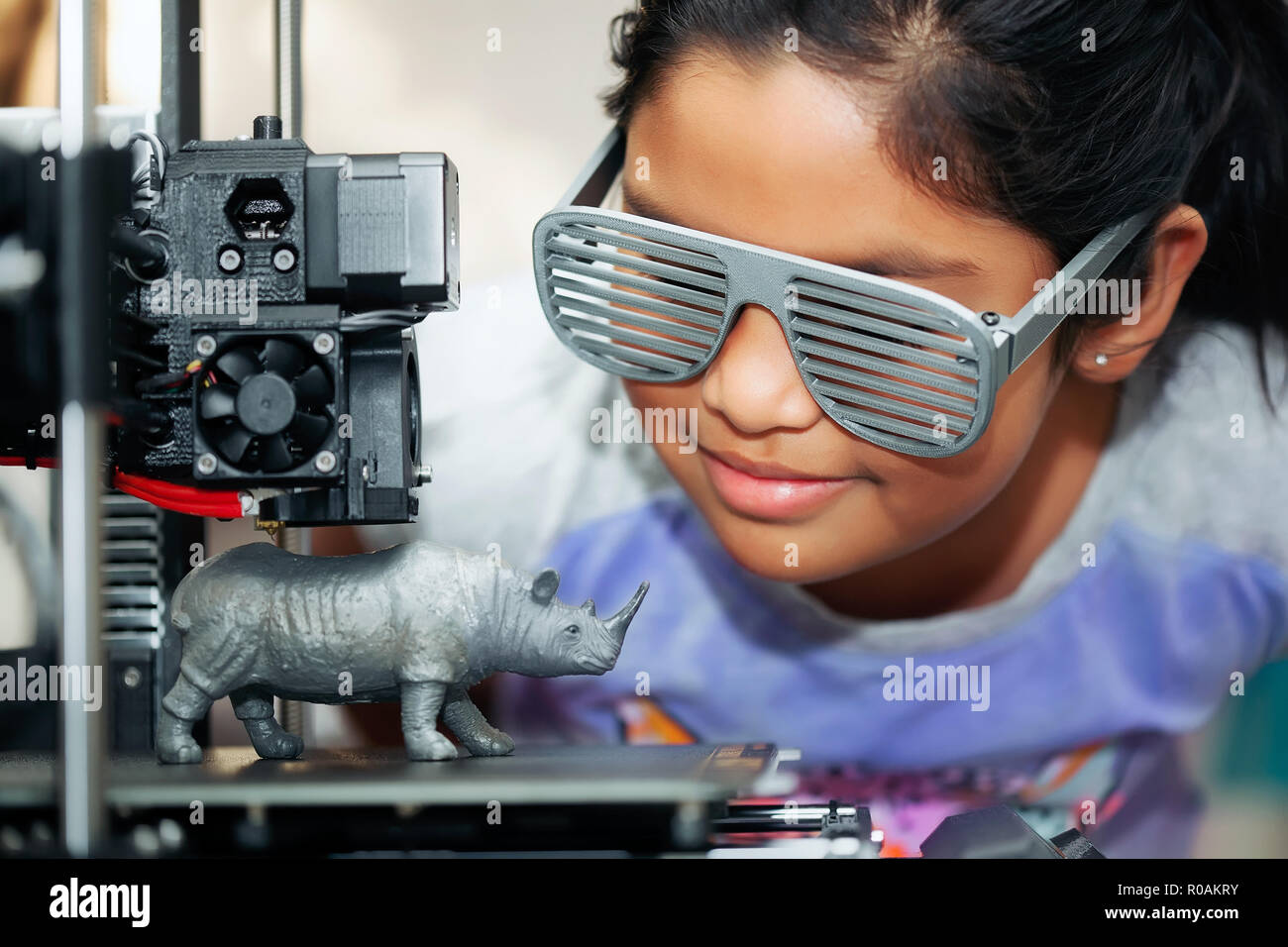 Ragazza carina con Cool 3D STAMPATA SHUTTER SHADES è guardare la sua stampante 3d come si stampa il suo modello 3d di un rinoceronte. Foto Stock