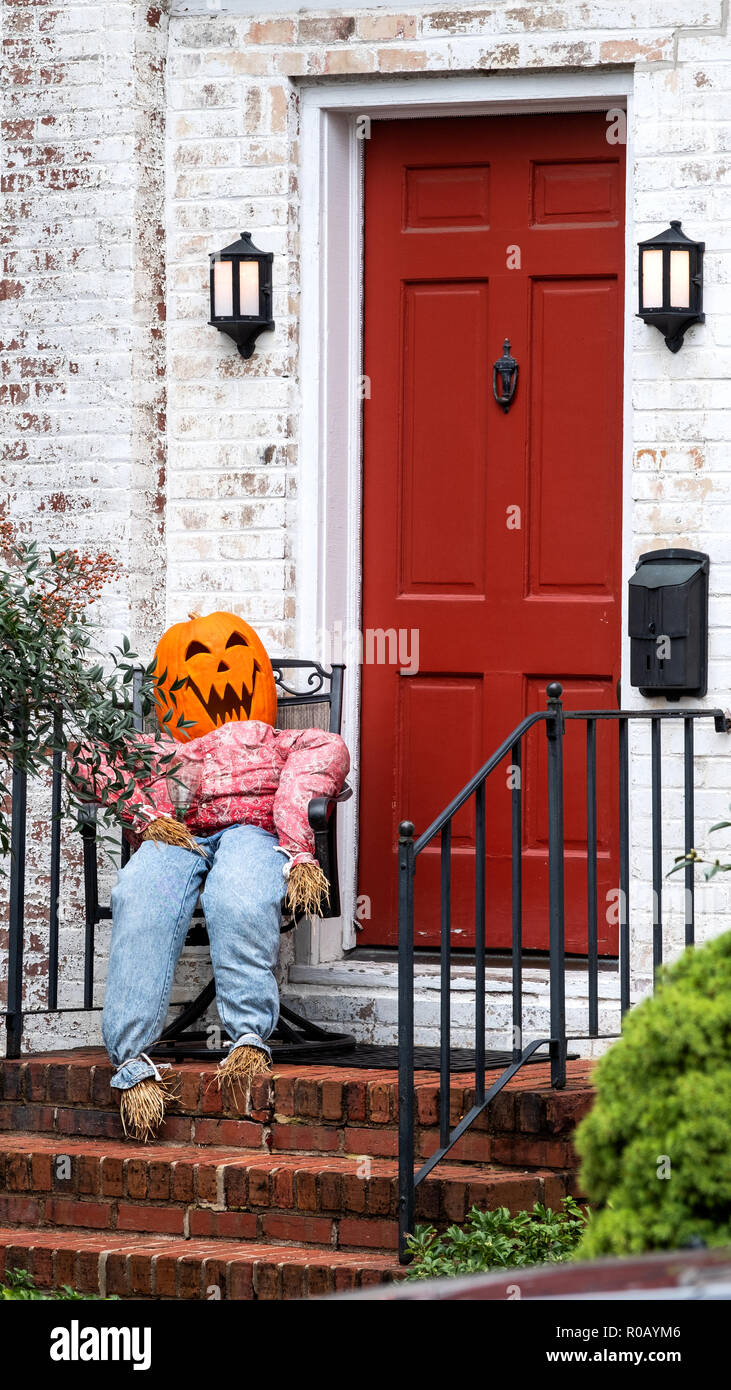 Un personaggio di Halloween a grandezza naturale con testa di zucca, seduto su una sedia a dondolo fuori dalla porta d'ingresso di una proprietà domestica. Una scena di Halloween Foto Stock