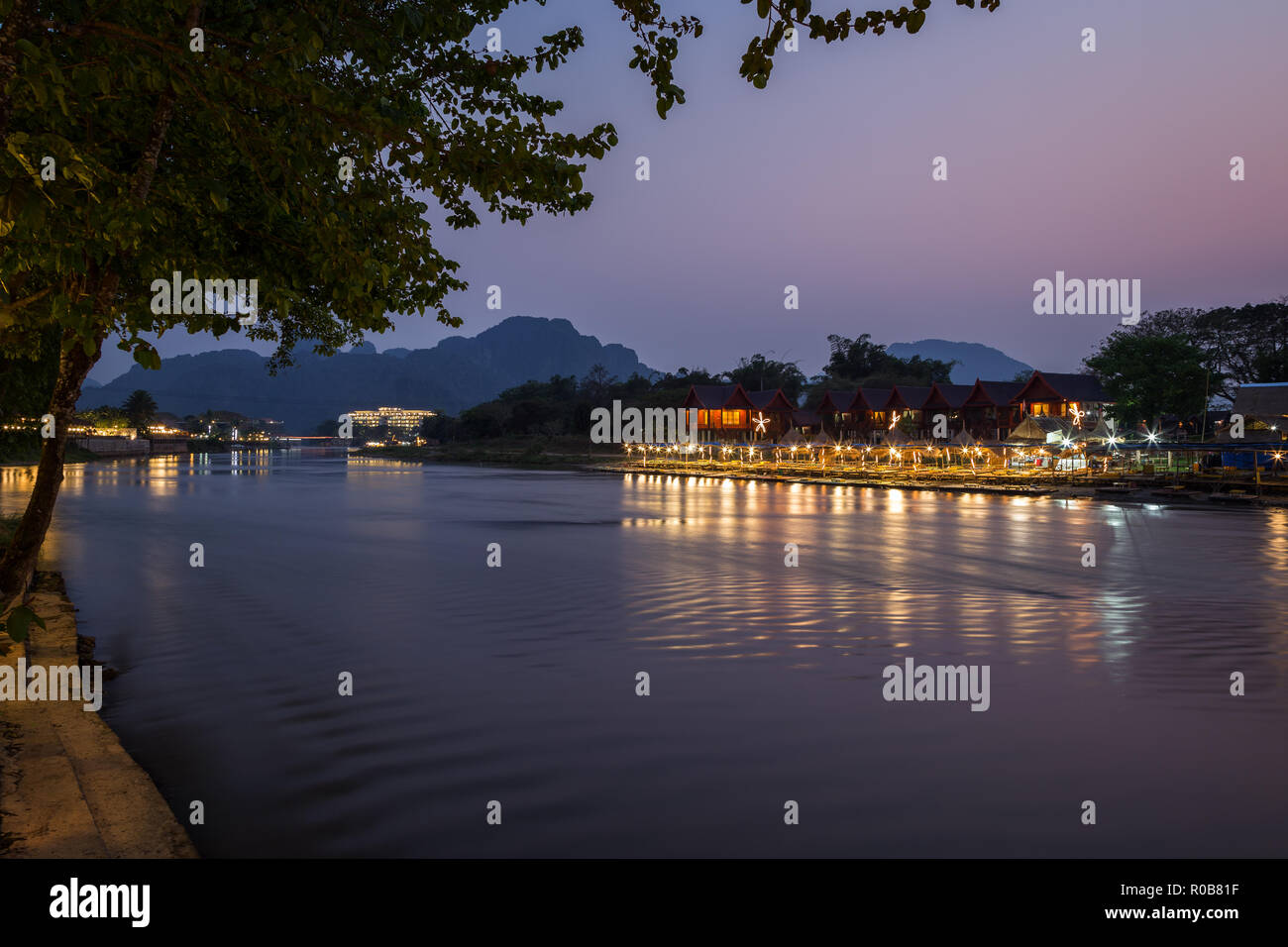Accesa waterfront restaurant, bungalows e gli edifici e le loro riflessioni sul Nam Song Rvier in Vang Vieng, Provincia di Vientiane, Laos, al tramonto. Foto Stock